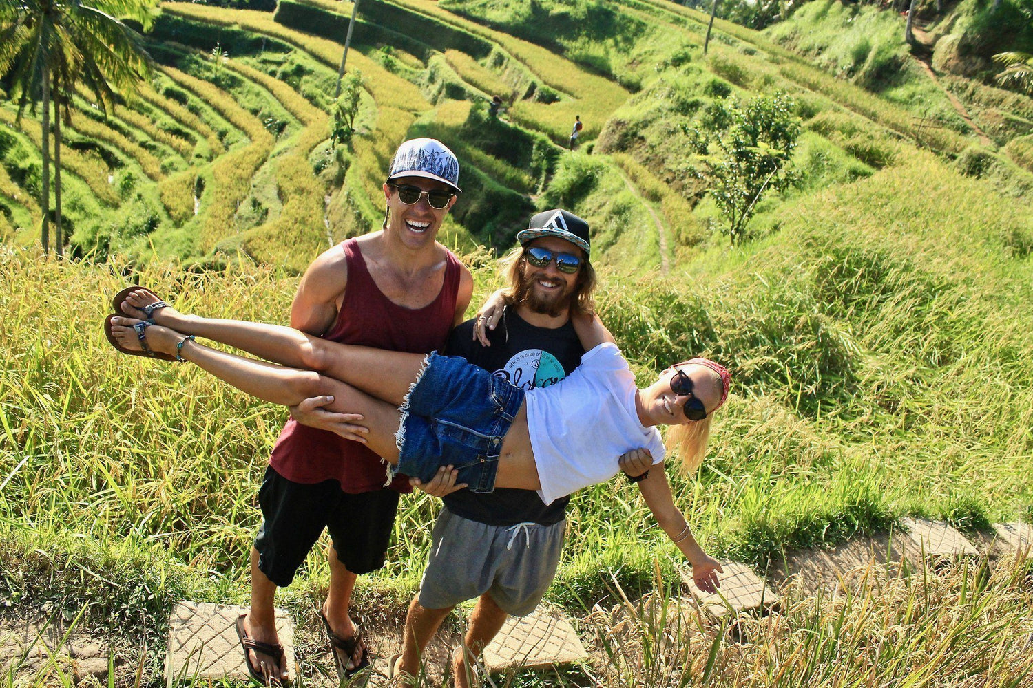 Photo of 2 people holding a person sideways in a scene green area