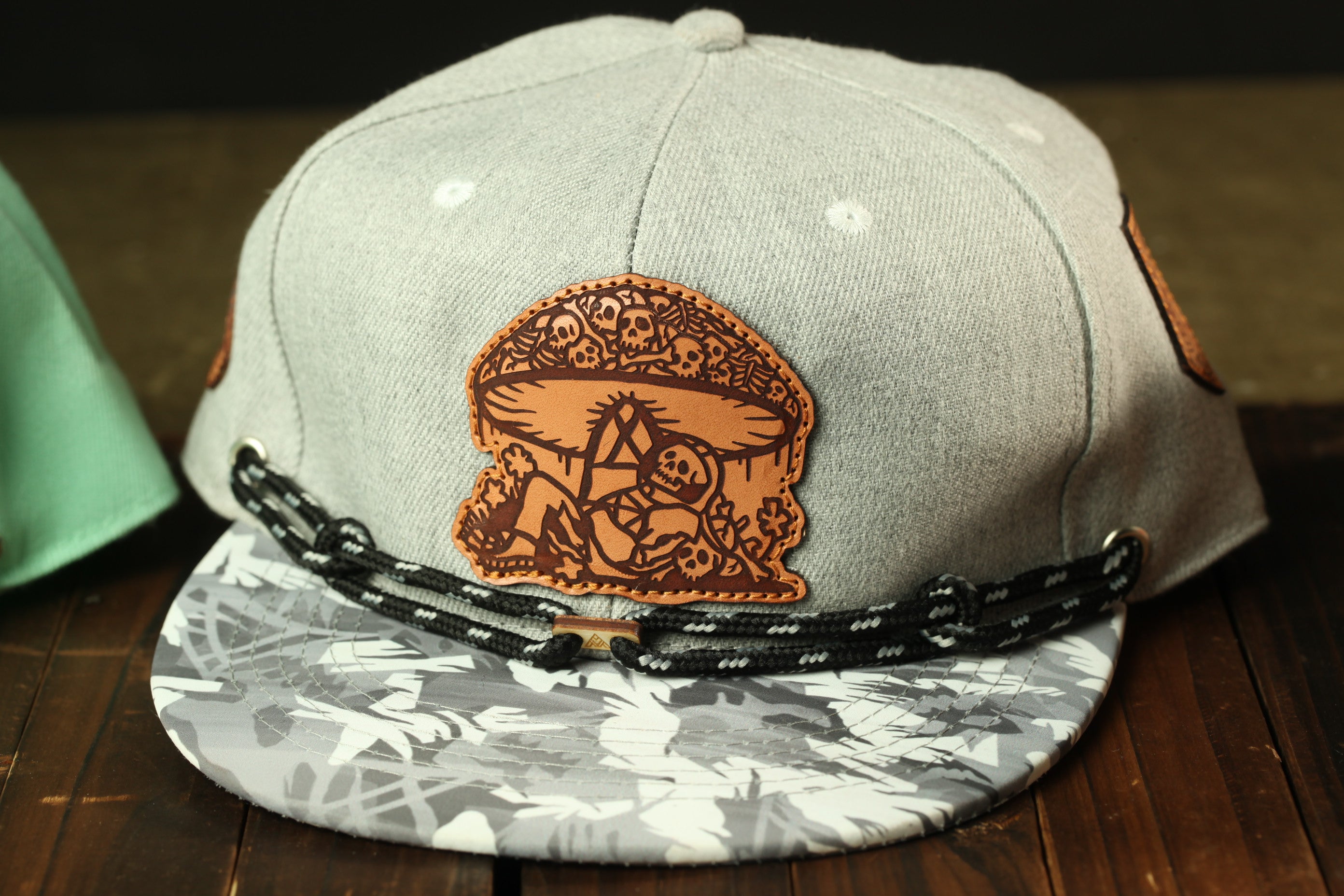 A gray baseball cap with a brown leather patch featuring a skull and crossbones design, placed on a wooden surface.
