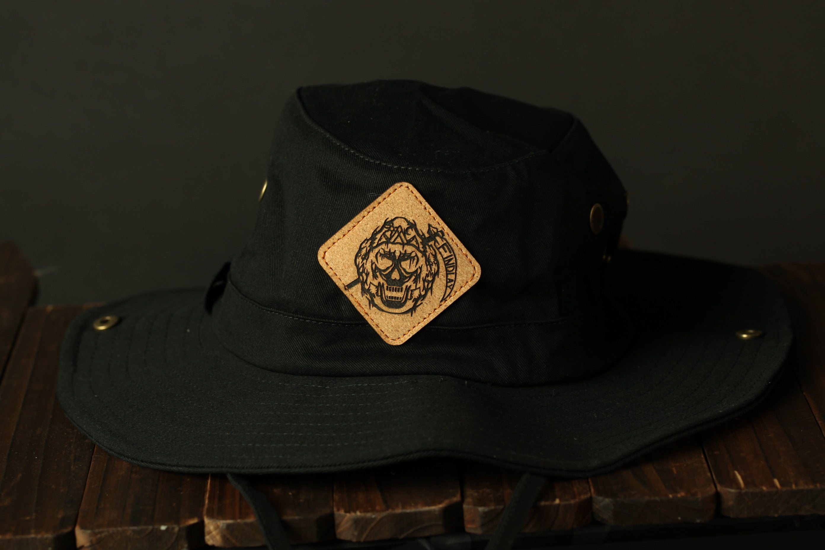 A black bucket hat with a skull patch on the front, placed on a wooden surface.