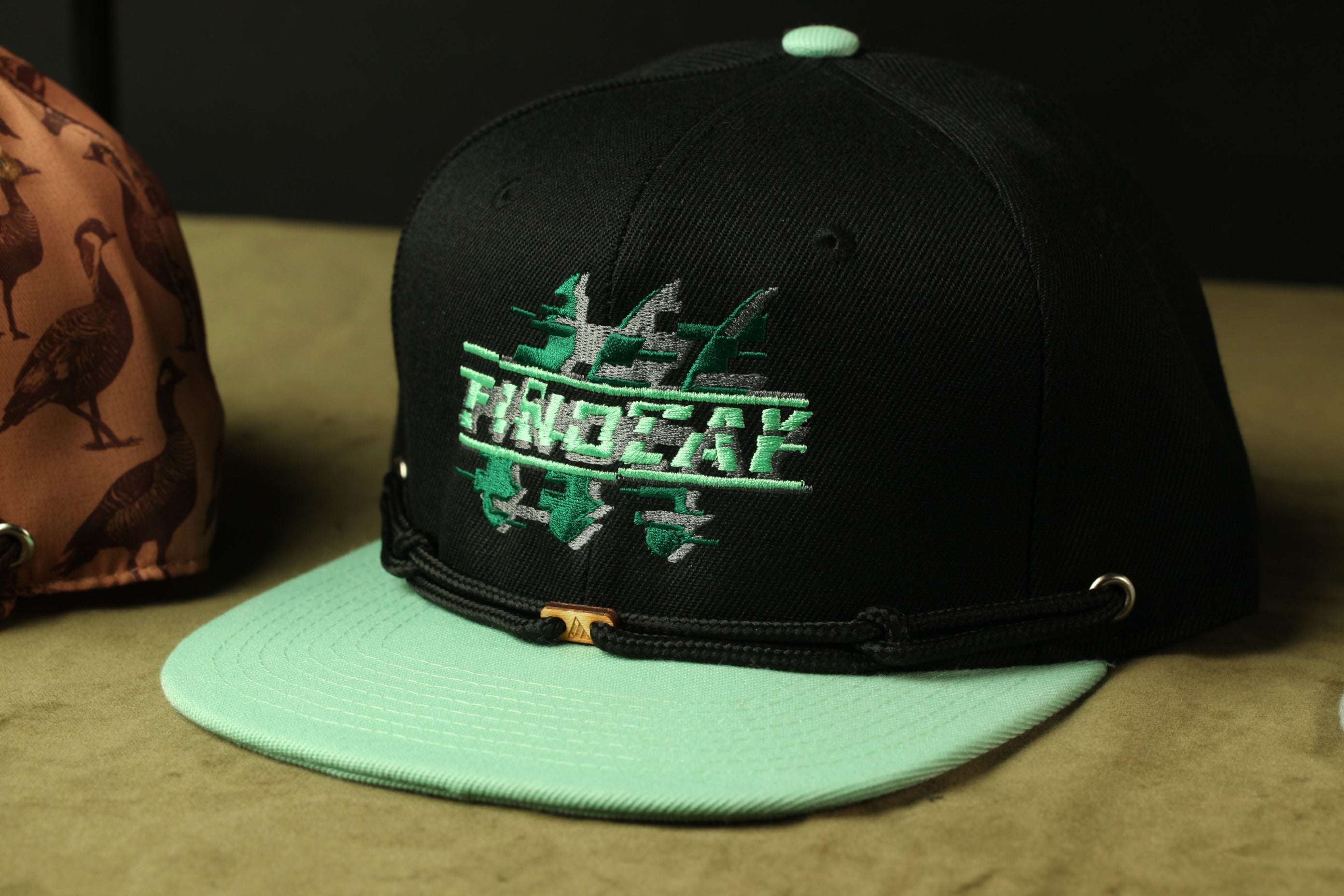 A black baseball cap with a green brim and a graphic design on the front, placed on a surface.