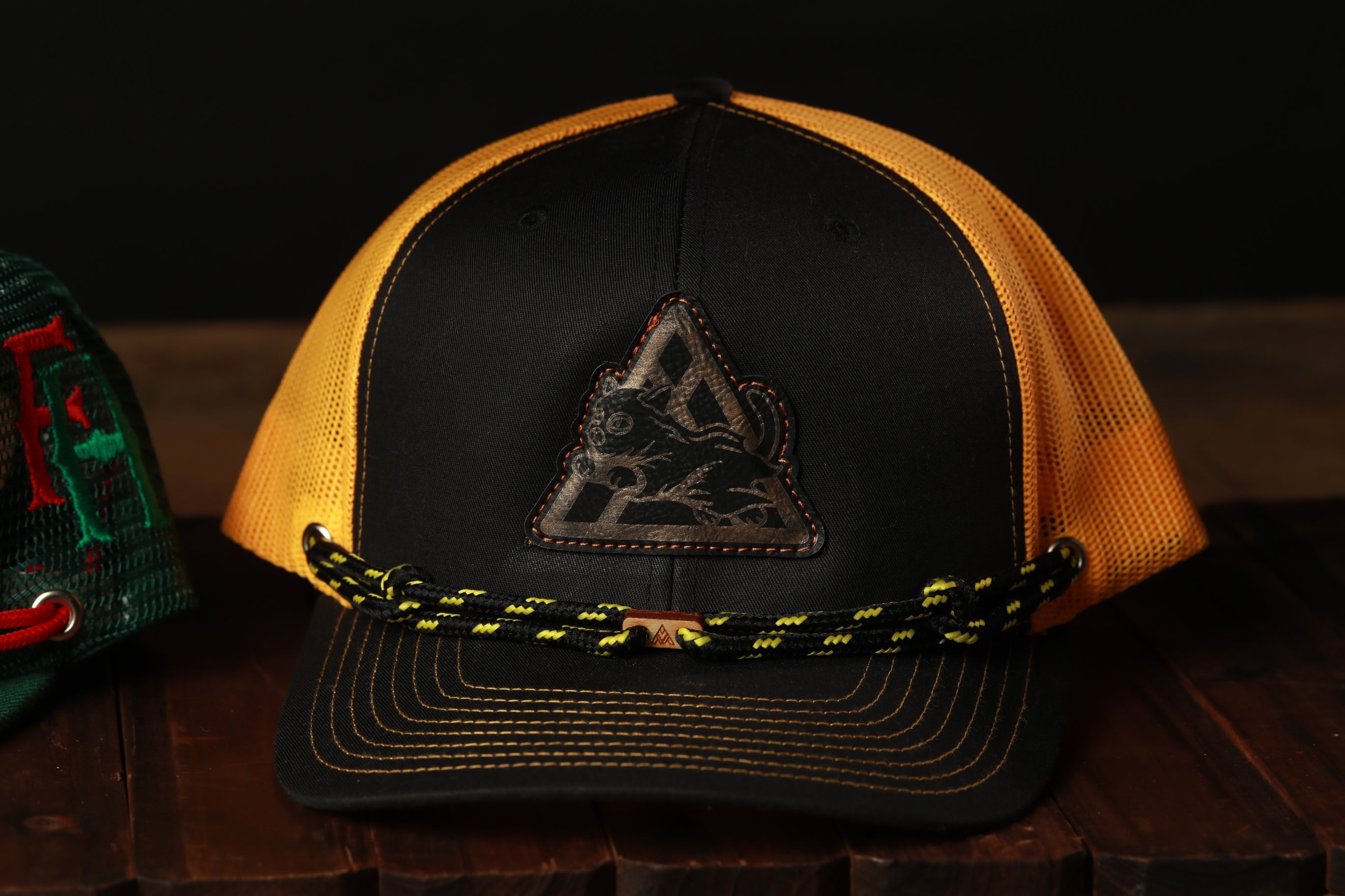 A black and yellow baseball cap with a black and yellow braided strap is displayed on a wooden surface.