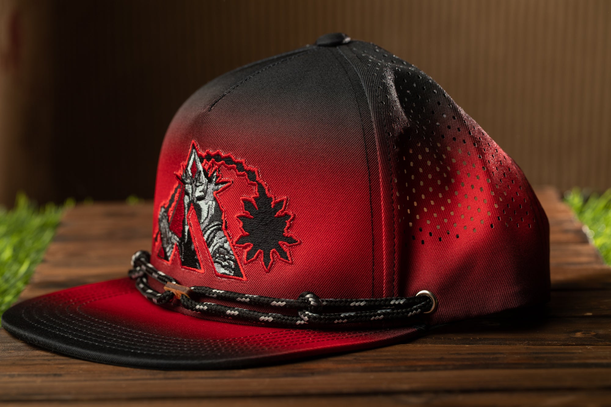 A red and black baseball cap with a black and white graphic design on the front, sitting on a wooden surface.