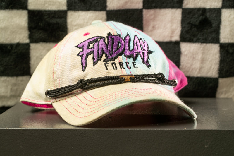 A white baseball cap with purple and pink text and a black strap, placed on a black surface against a checkered background.