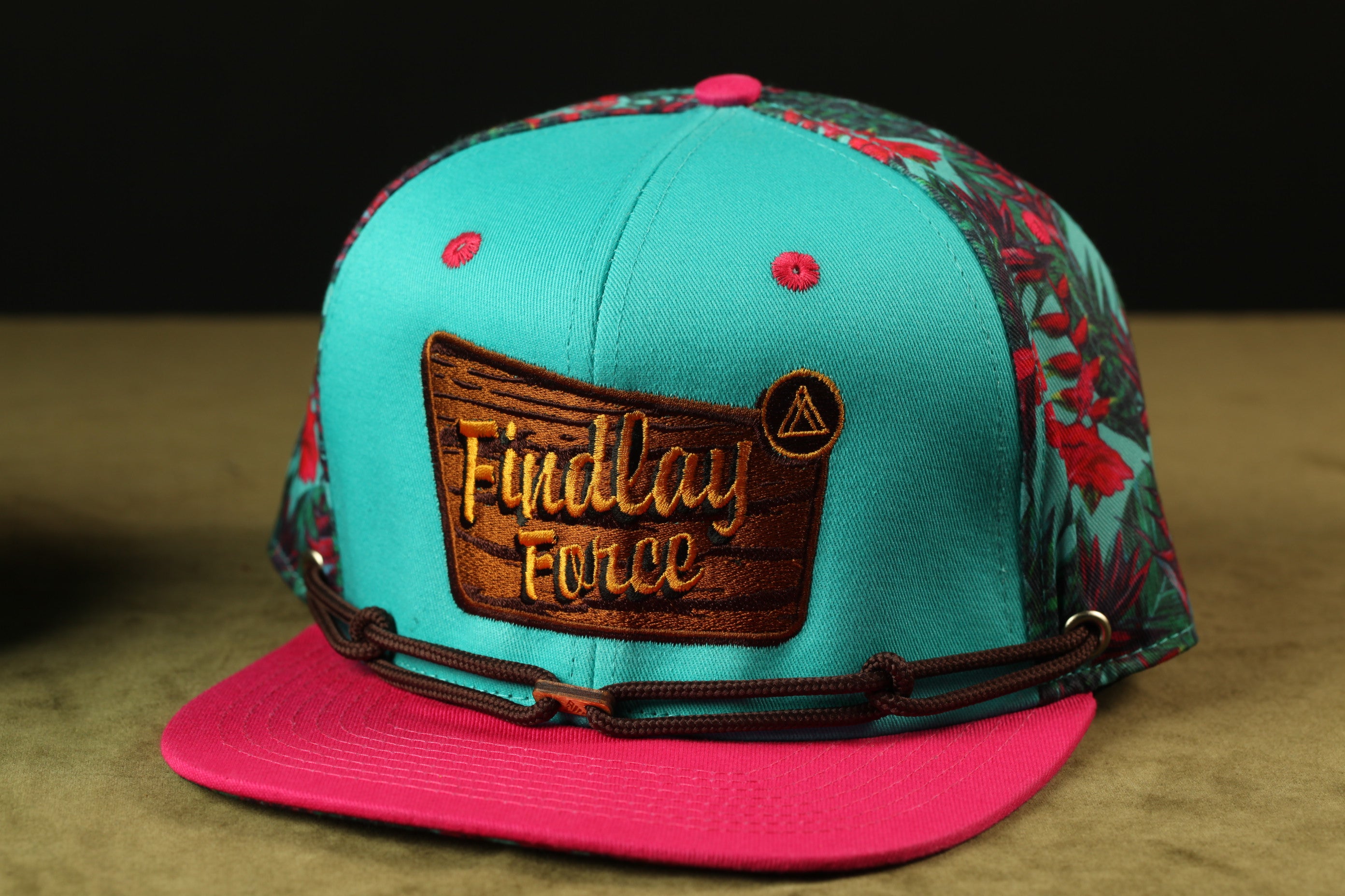 A turquoise baseball cap with a floral pattern and the text "Findlay Force" printed on it.