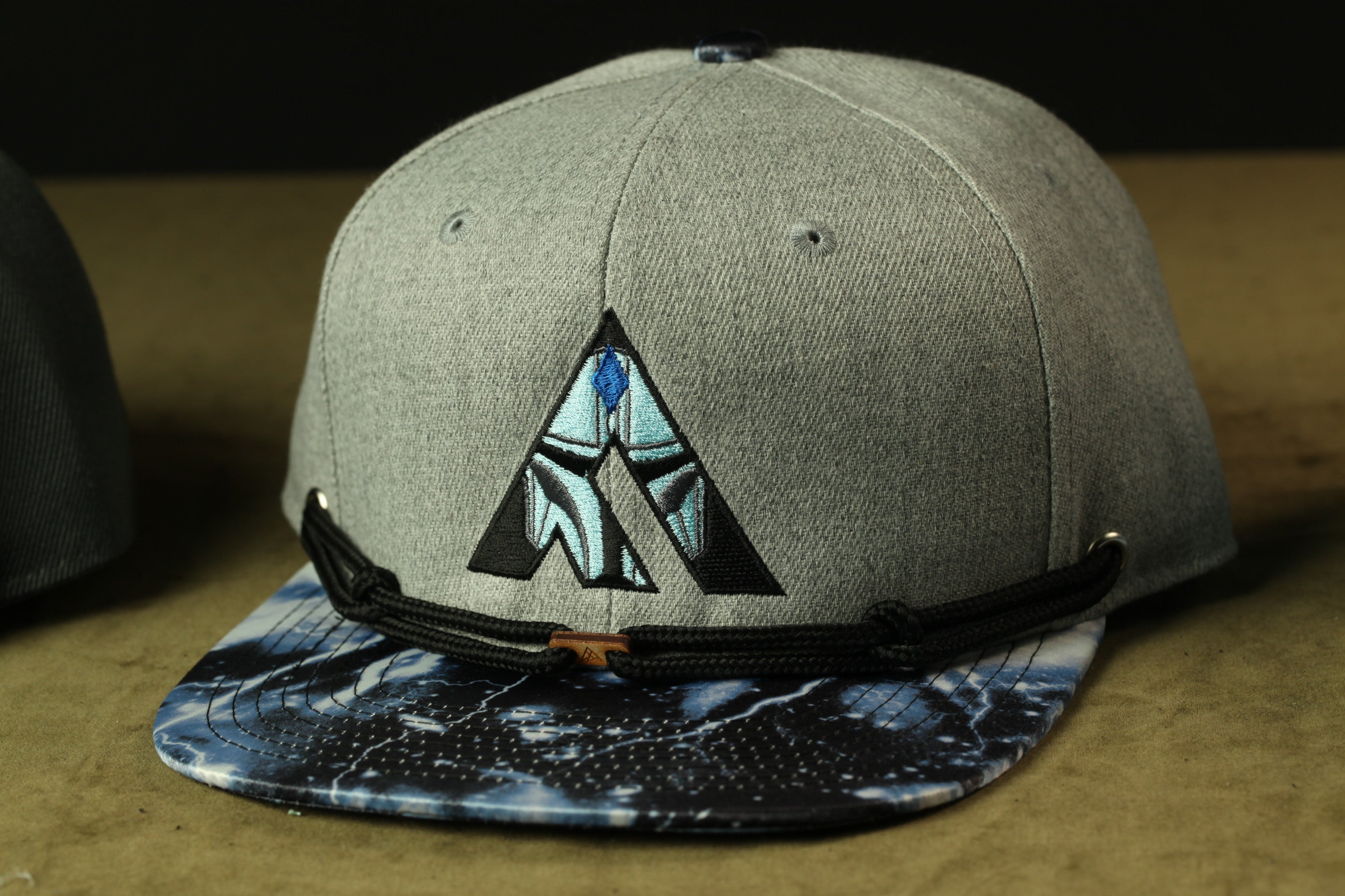 A gray baseball cap with a blue and black patterned brim and a black strap.