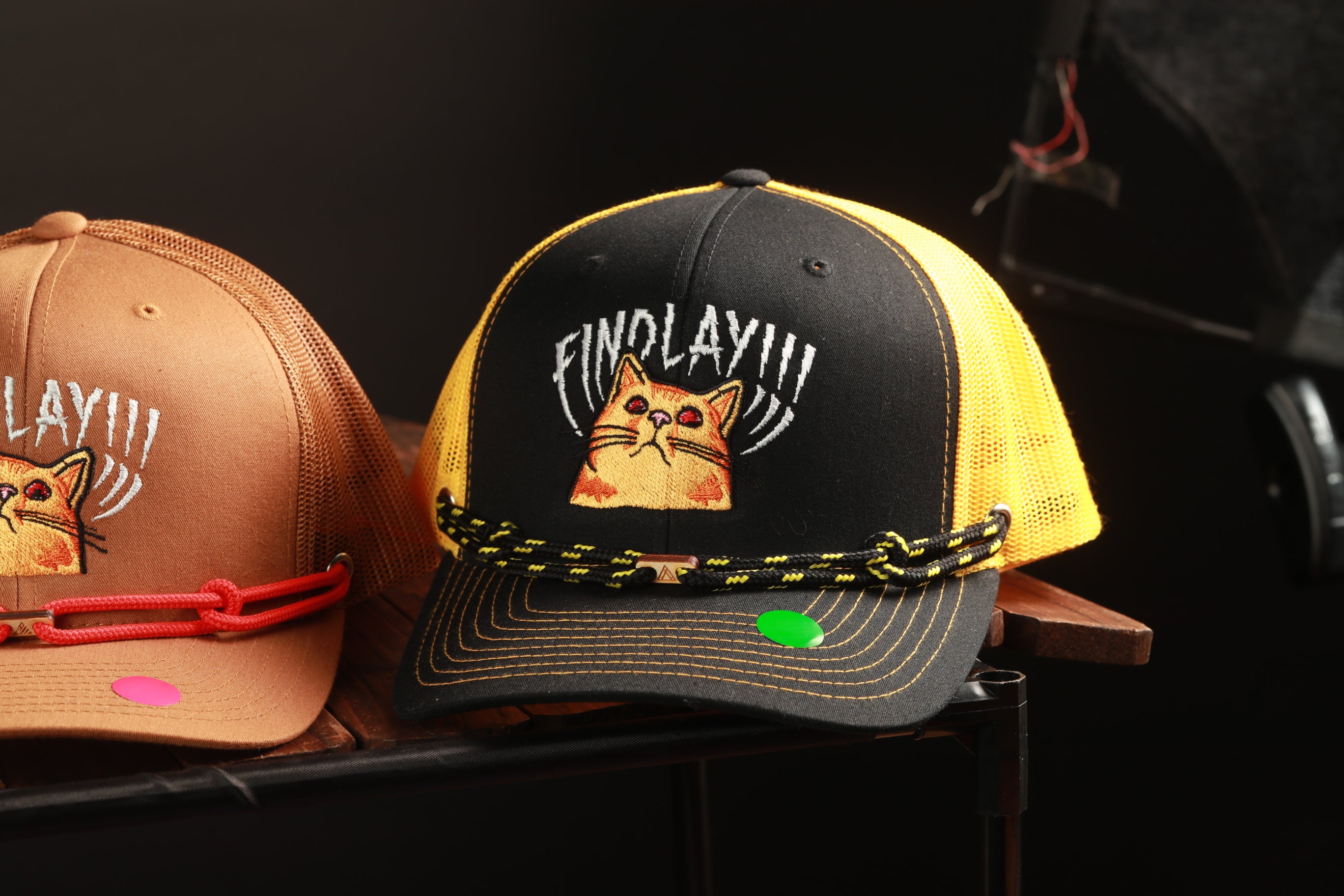 Two baseball caps with cat designs, one black and one yellow, are displayed on a shelf.