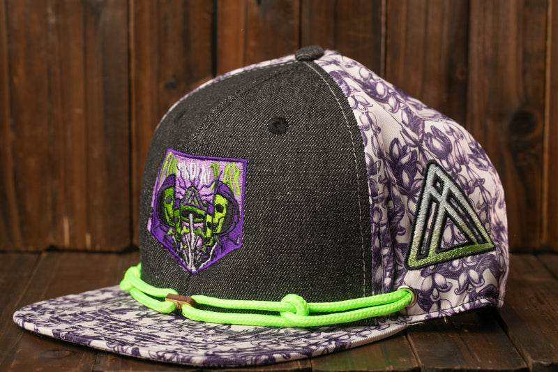 A black and purple baseball cap with a floral pattern and a skull-like design on the front, sitting on a wooden surface.