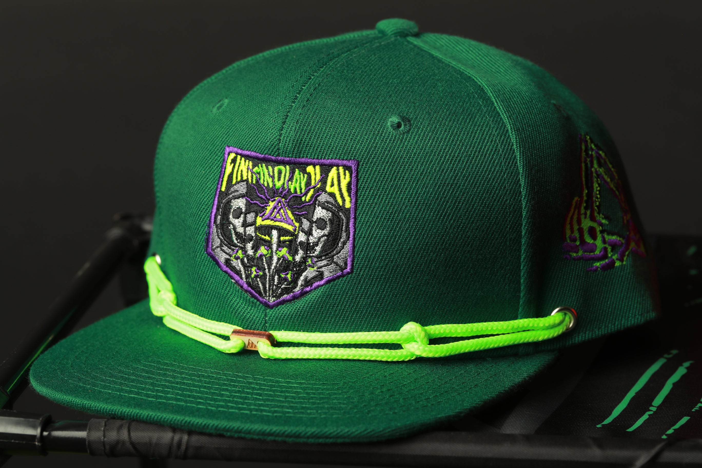 A green baseball cap with a purple and yellow design on the front, featuring a skull and crossbones motif.