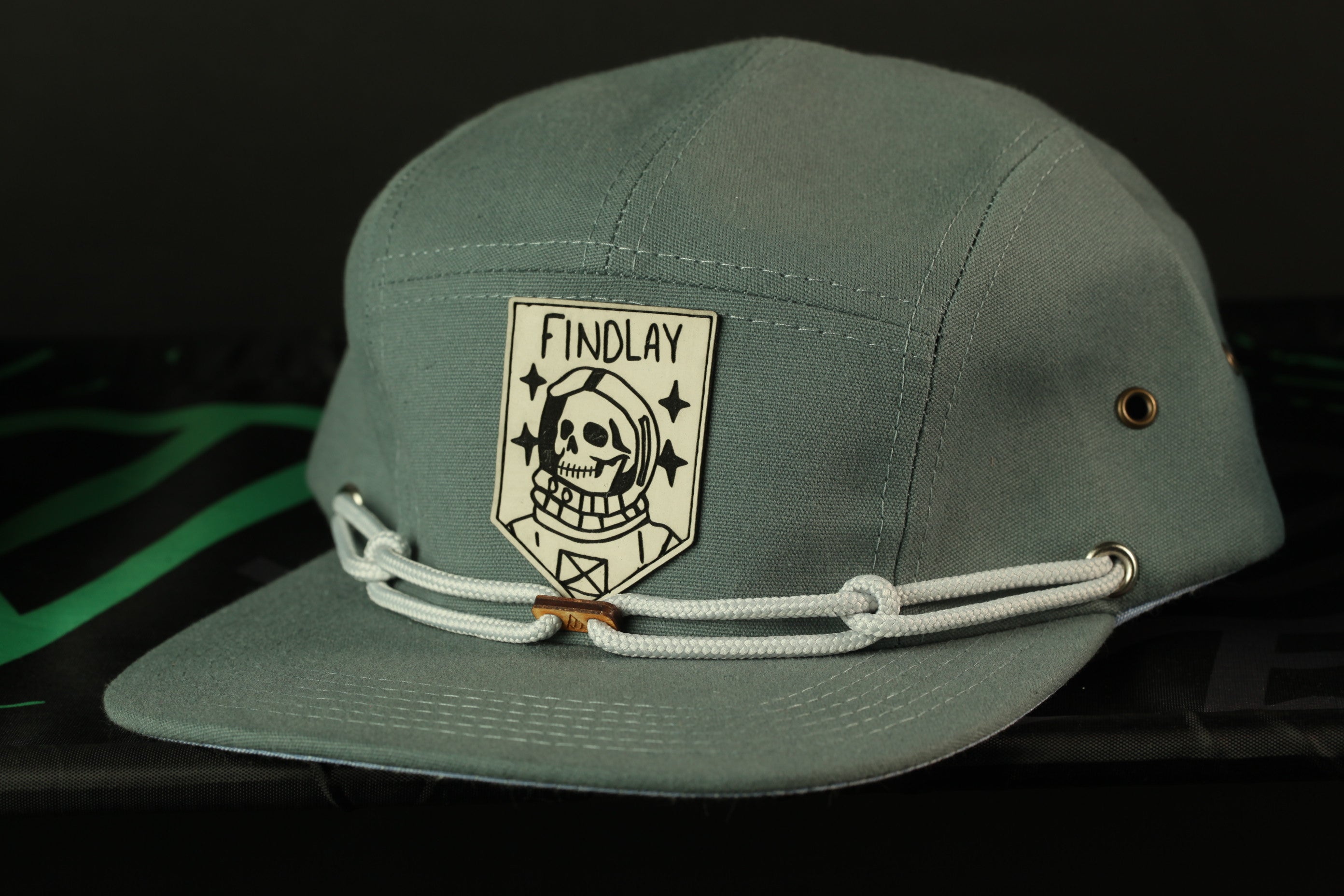 A gray baseball cap with a white skull and crossbones design and the text "FINDLAY" printed on it.