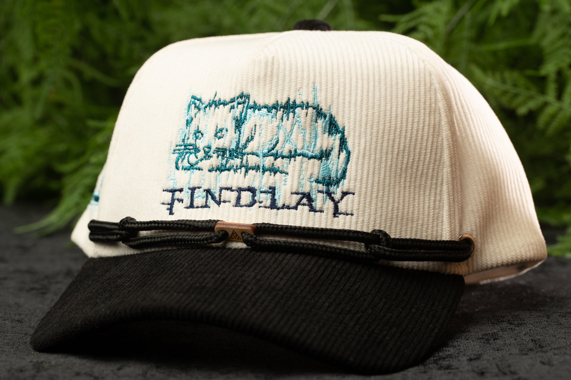 A white baseball cap with a black brim and a black band, featuring a blue embroidered cat design and the word "FINDlay" printed on it.