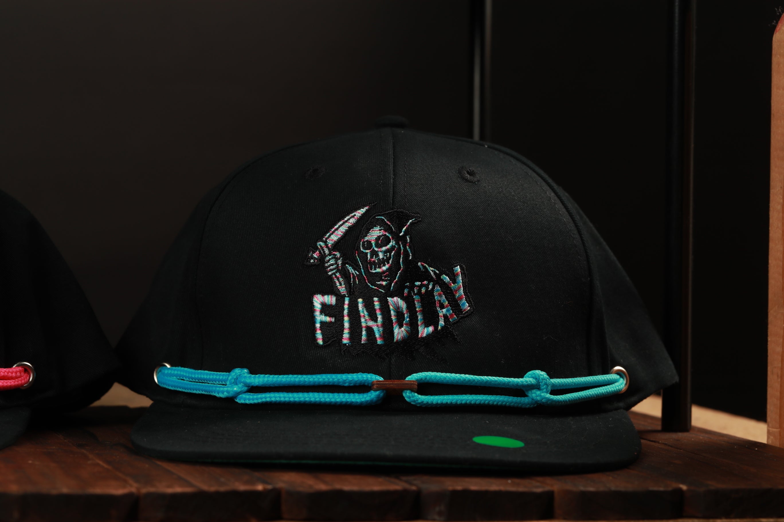 A black baseball cap with a skull and crossbones design and the word "FINDlay" printed on it, sitting on a wooden surface.