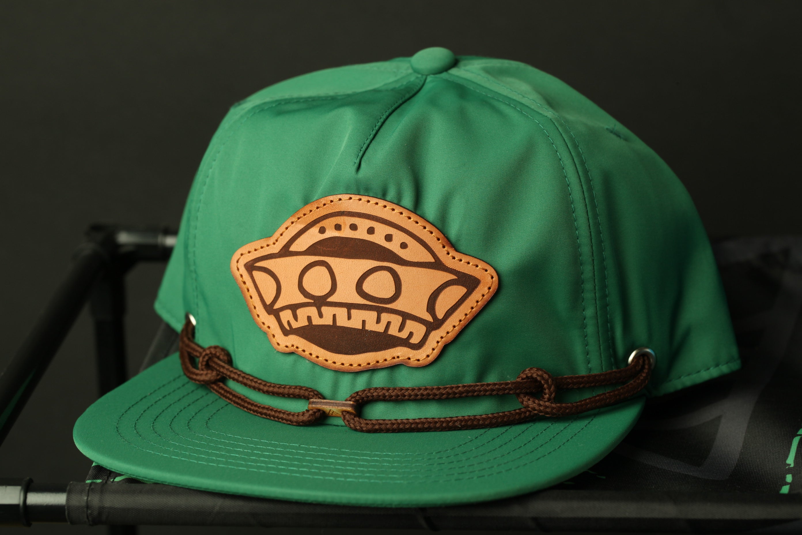 A green baseball cap with a brown leather patch featuring a cartoon character on it, placed on a black surface.