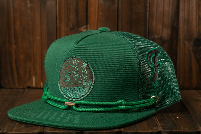 A green baseball cap with a circular logo on the front, sitting on a wooden surface.