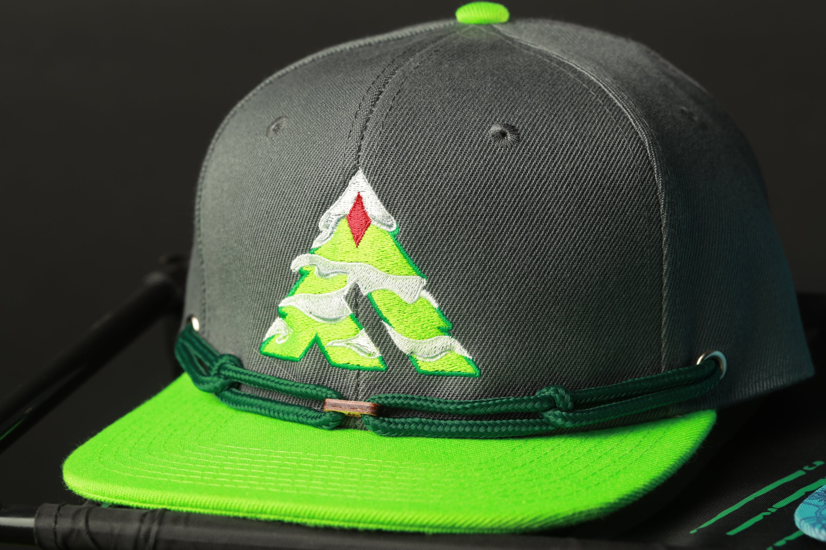A gray baseball cap with a green brim and a green and white logo on the front, placed on a black surface.
