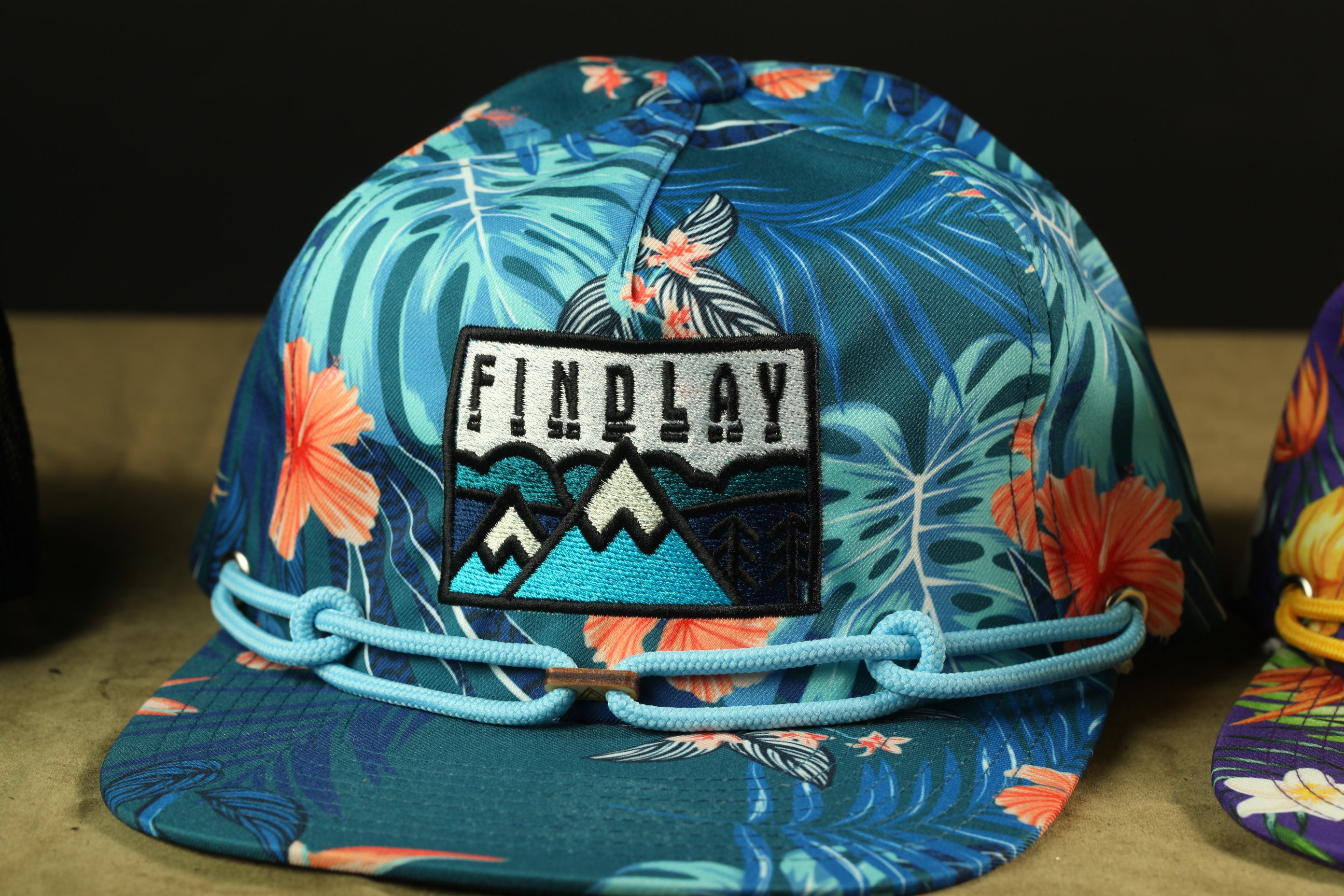A colorful floral print baseball cap with the word "FINDPLAY" printed on it.