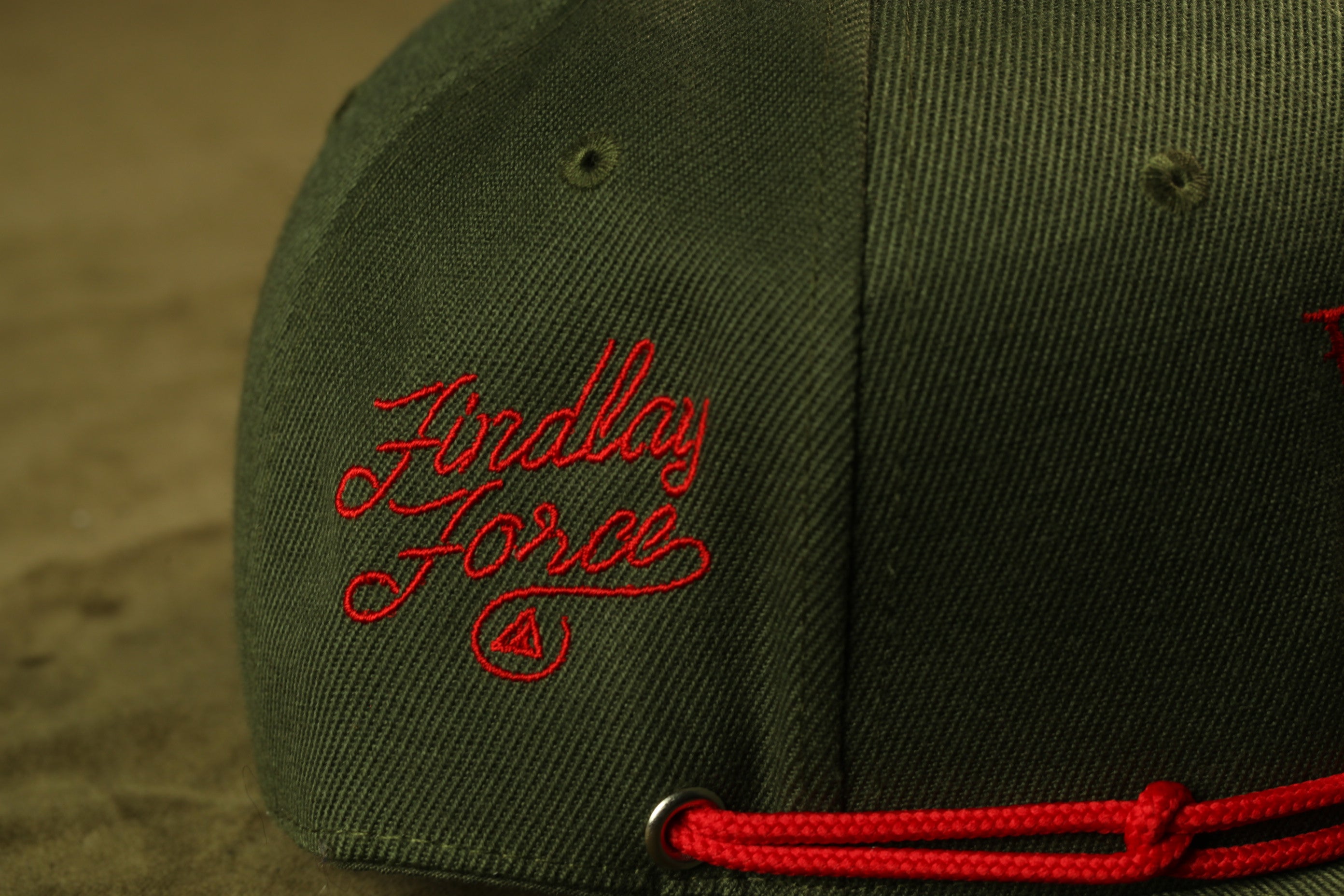 A close-up view of a green baseball cap with red embroidered text on the side.