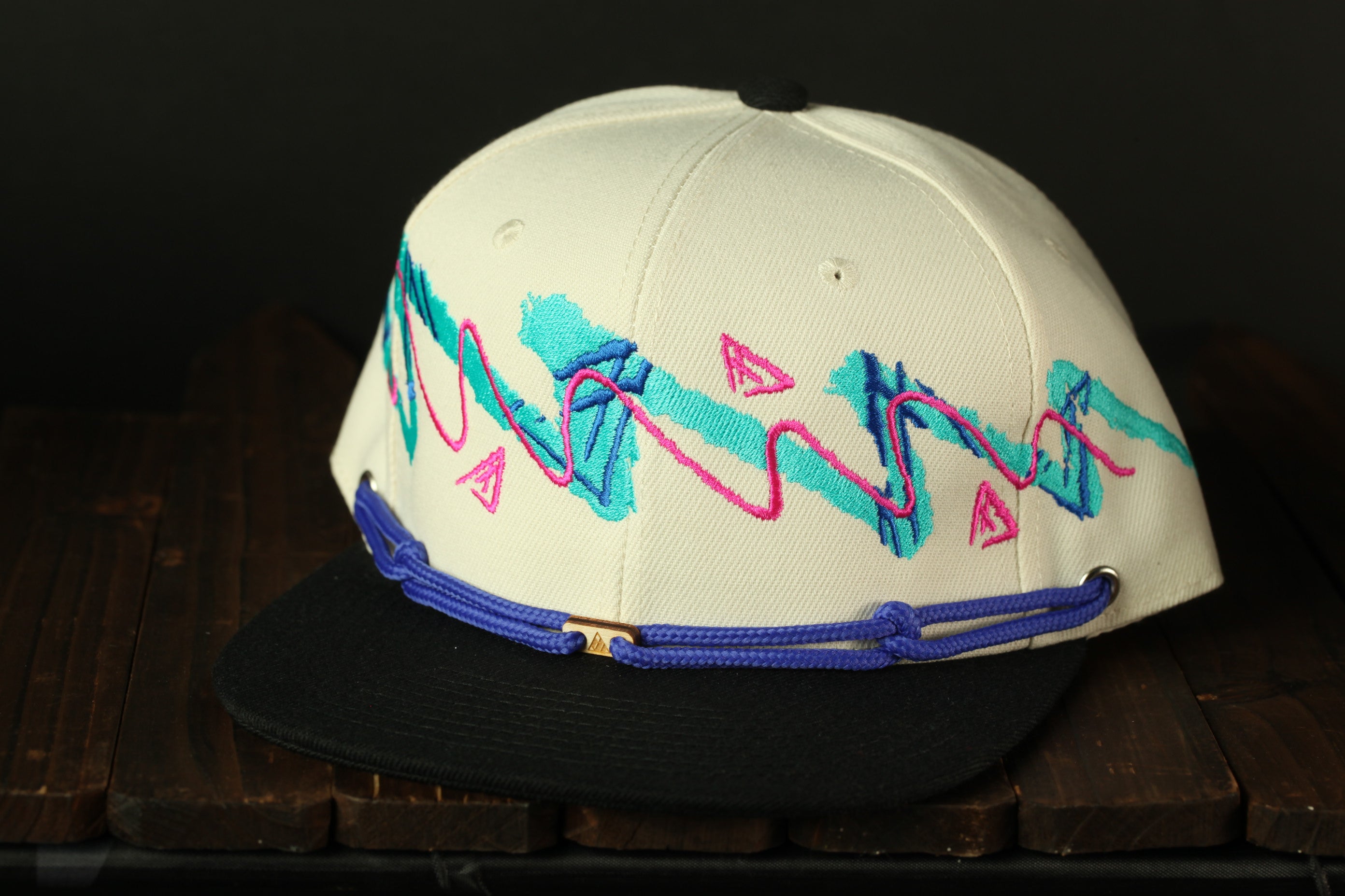 A white baseball cap with a black brim and a colorful, abstract design in pink, blue, and green on the front.