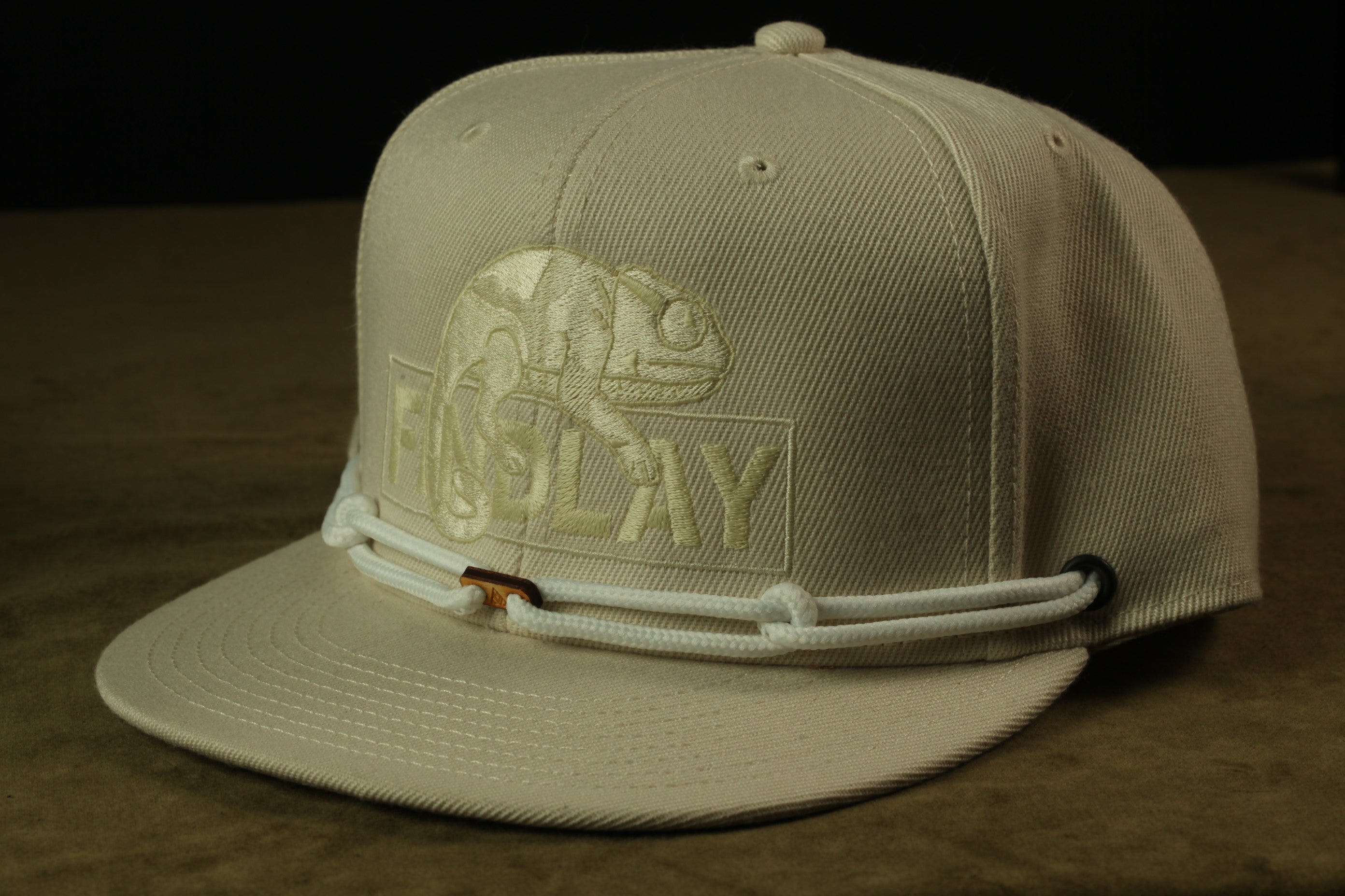 A beige baseball cap with a white logo and a white strap.