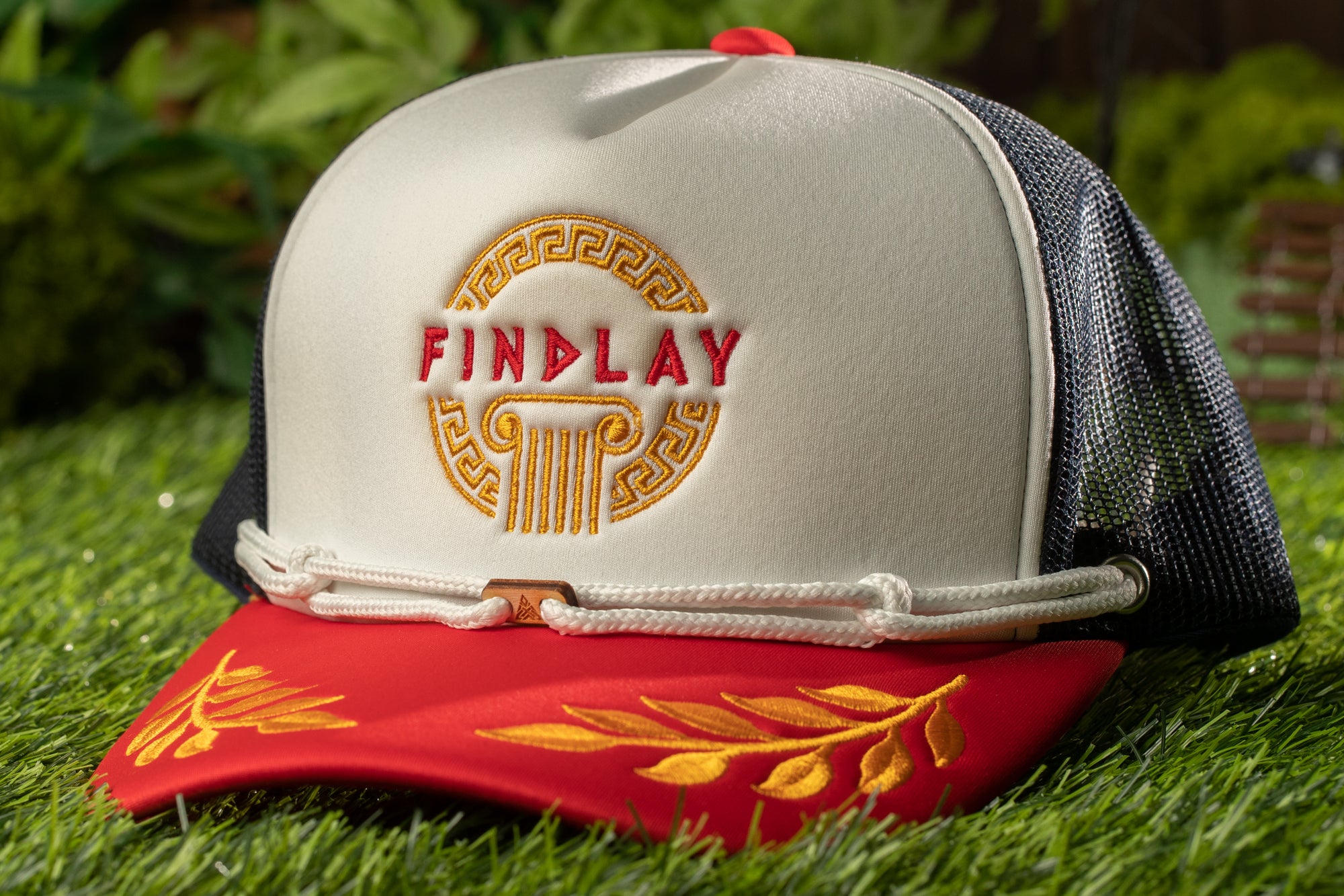 A white baseball cap with a red brim and gold leaf design, featuring the word "FINDLAY" in red letters on the front.
