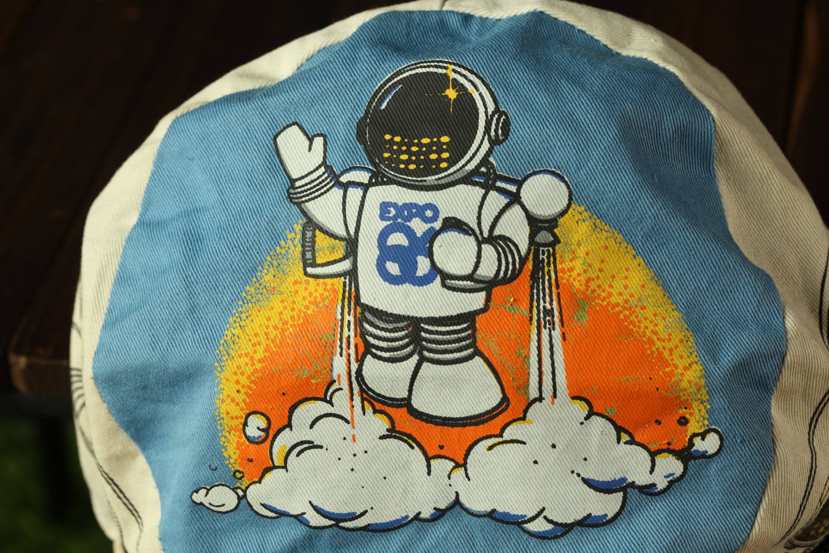 a blue and white cap with a cartoon astronaut on it, wearing a spacesuit and holding a rocket ship.