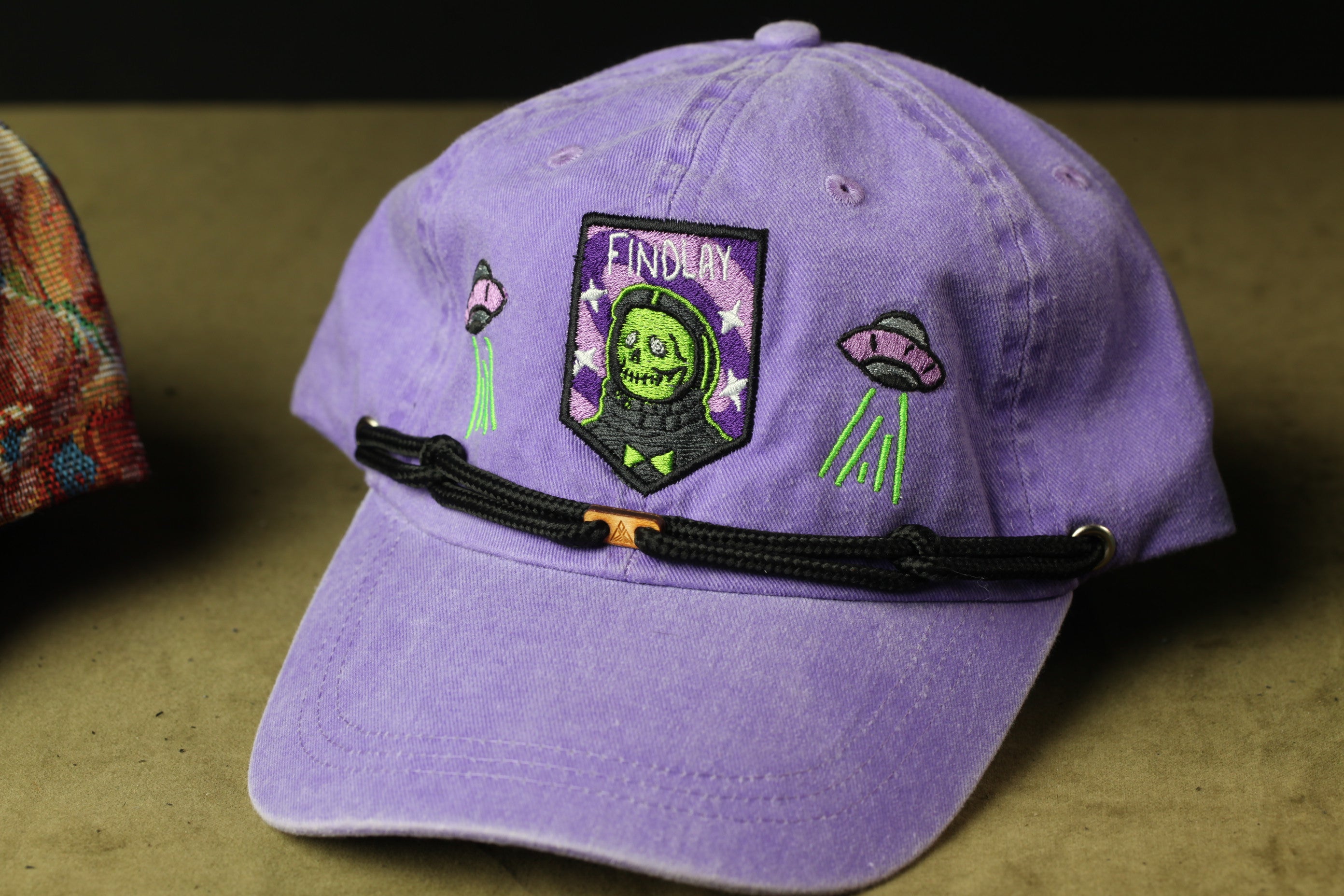 A purple baseball cap with a skull and green alien motif, featuring a patch with the word "FIND" and a graphic of a green alien.