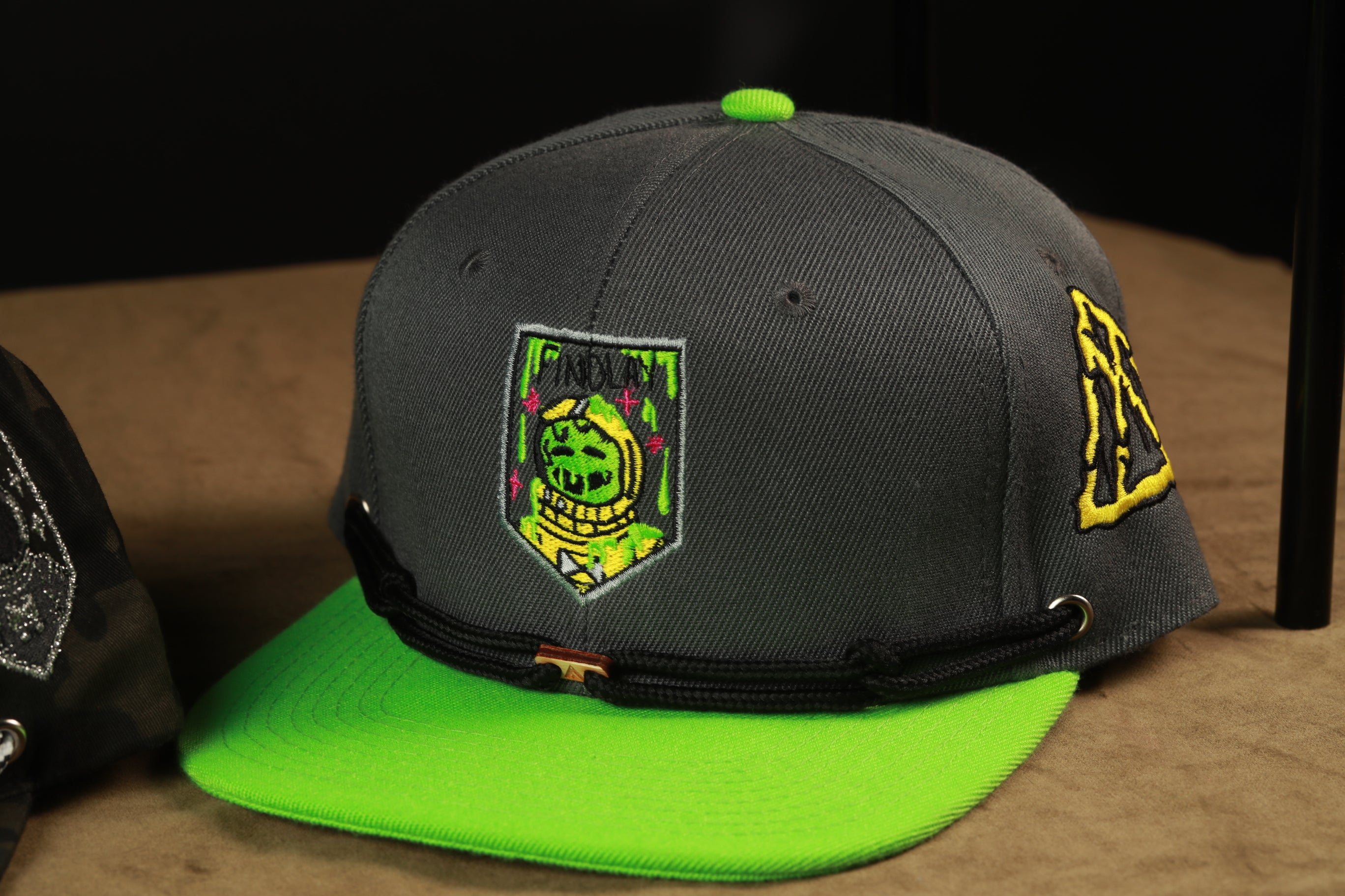 A black baseball cap with a green brim and a patch on the front, sitting on a brown surface.