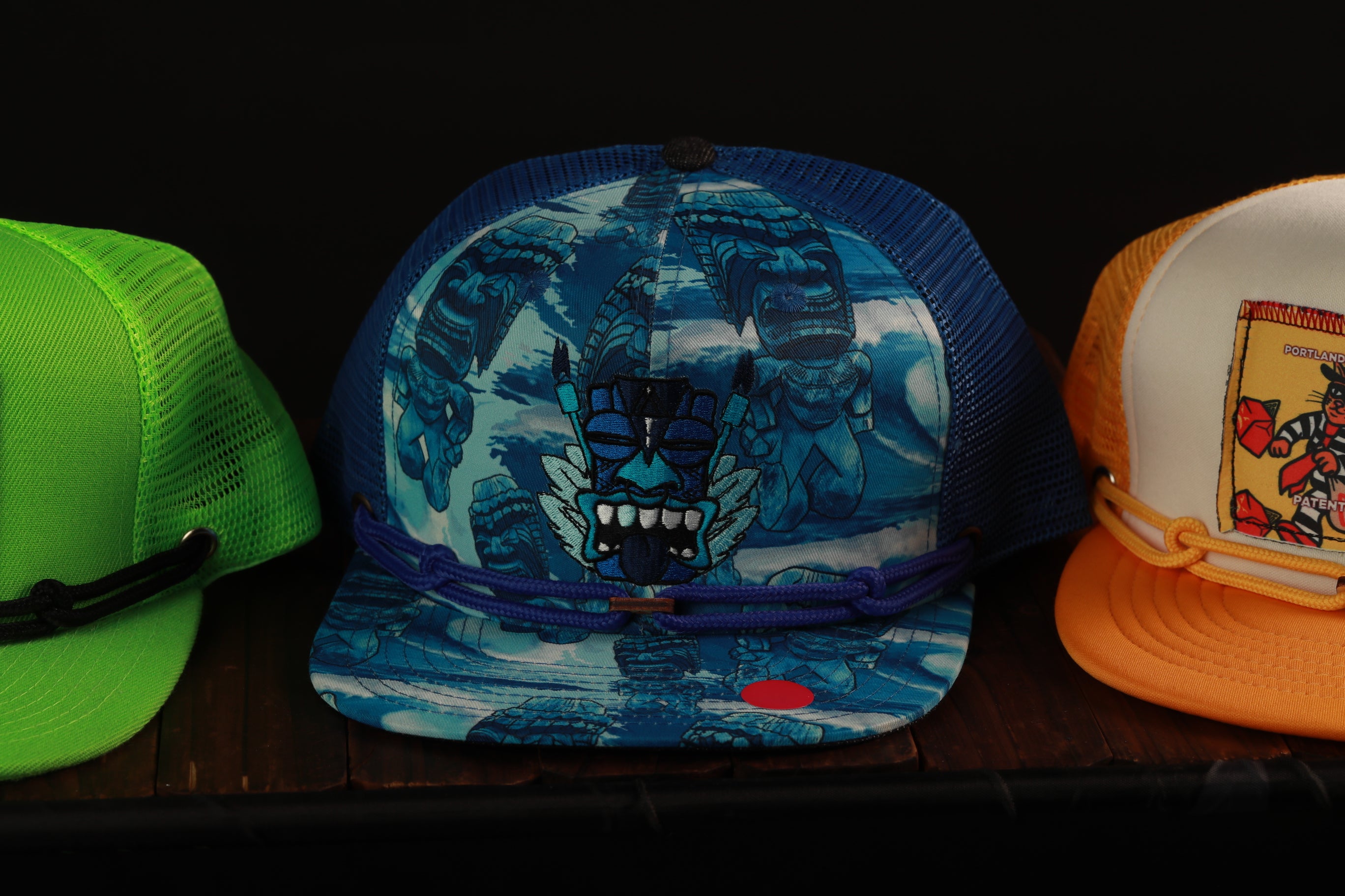 Three colorful baseball caps are displayed on a shelf, each with unique designs and patterns.