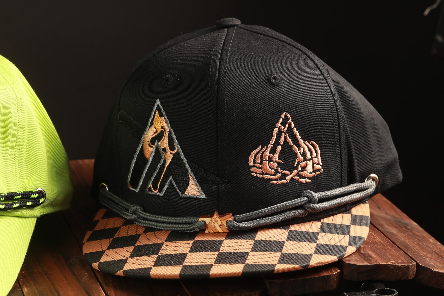 A black baseball cap with a checkered pattern and a graphic design on the front, placed on a wooden surface.