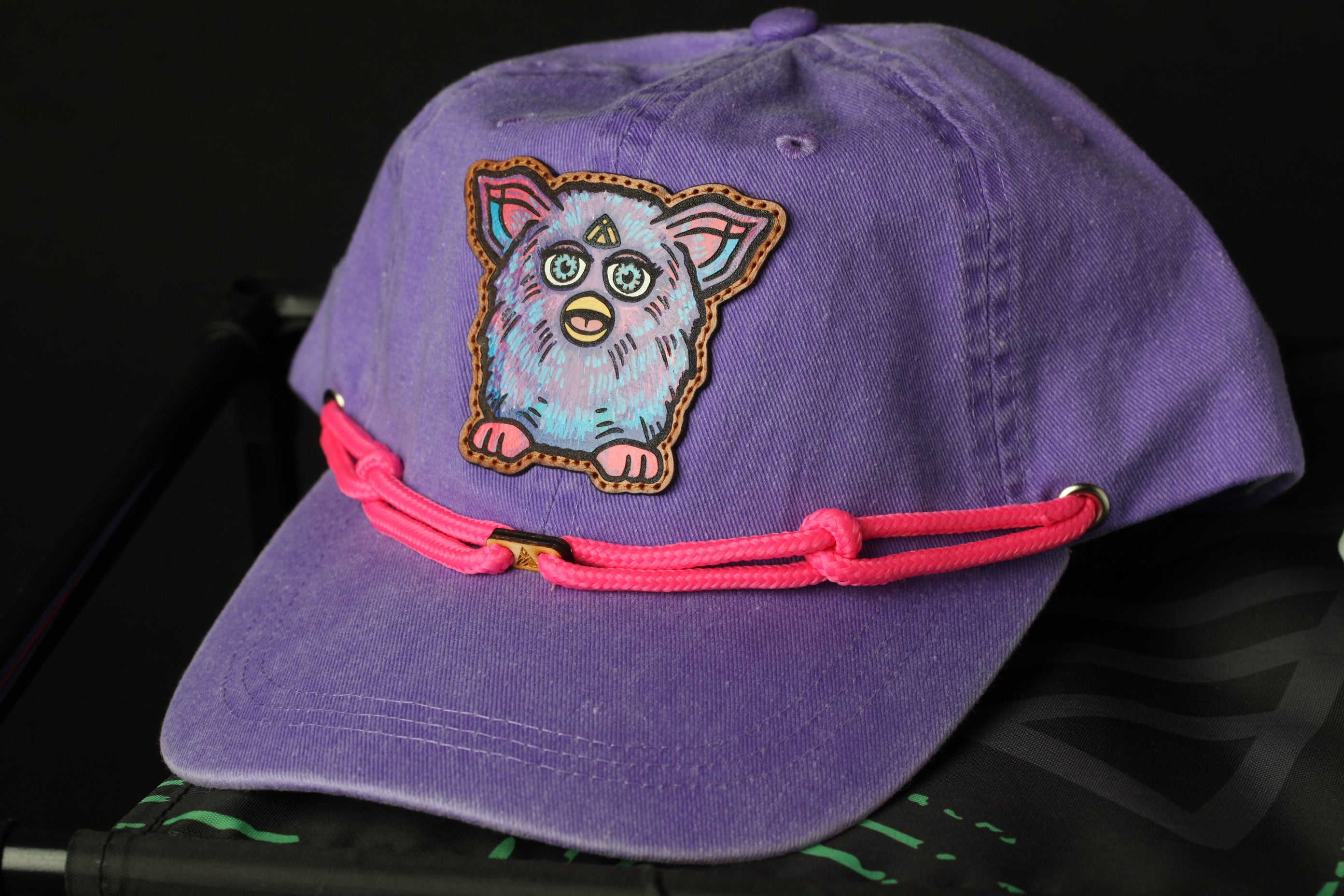 A purple baseball cap with a pink braided strap and a cartoon character design on the front.