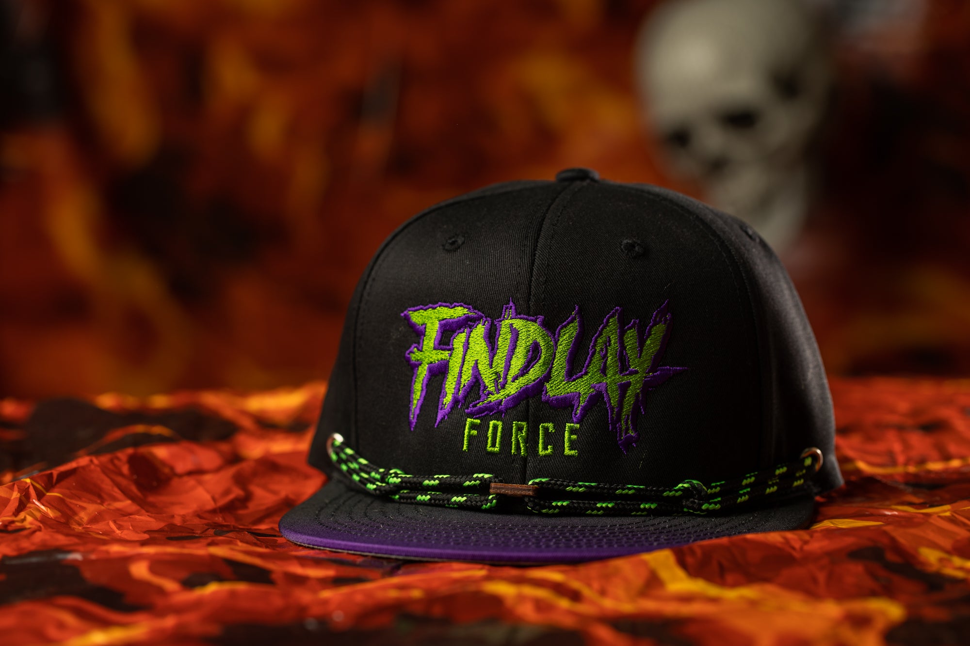 A black baseball cap with the text "FINDLAY FORCE" printed on it, placed on a red and orange patterned surface.
