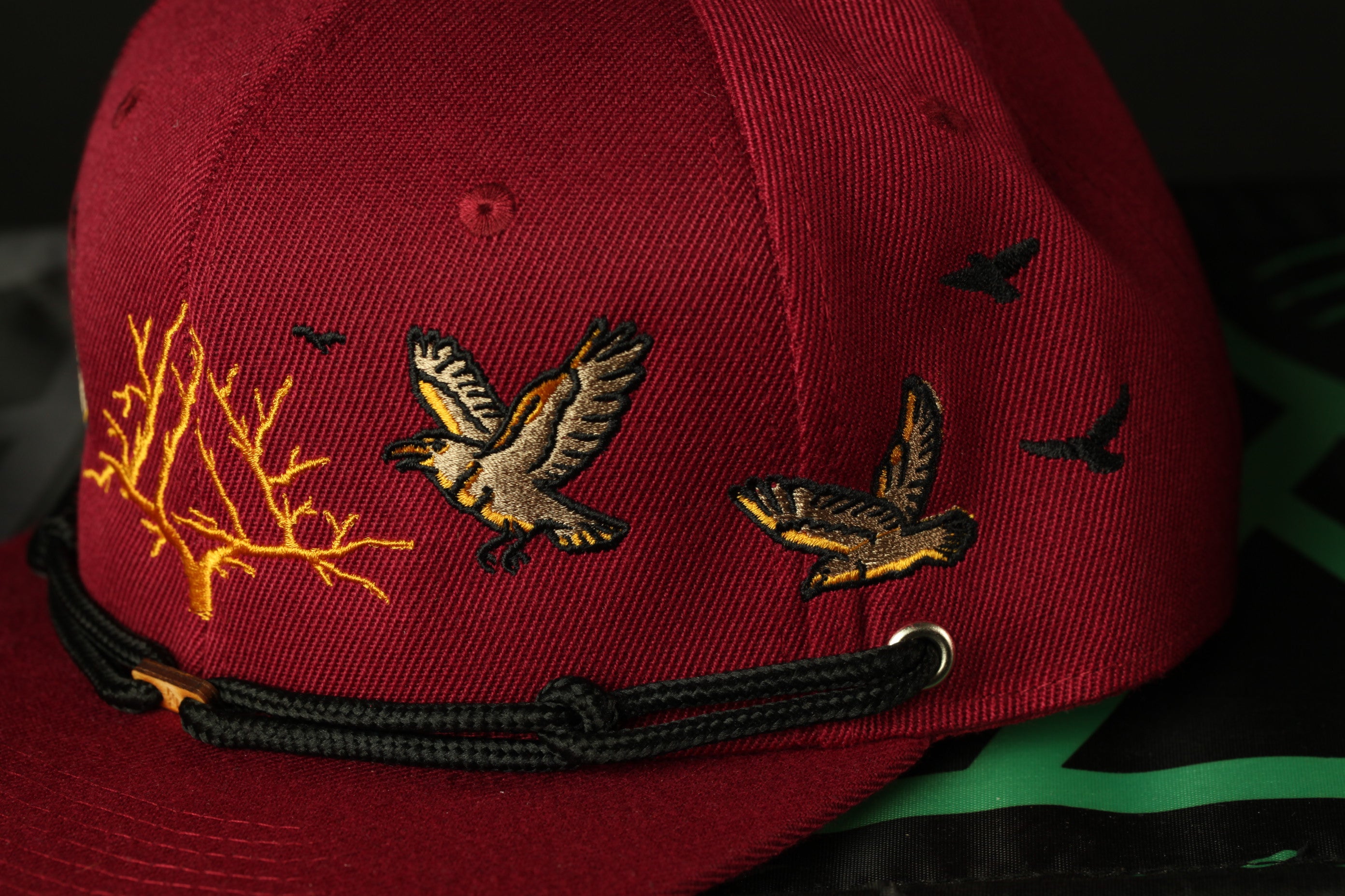 A close-up view of a red baseball cap with a black band and embroidered images of birds on the front.