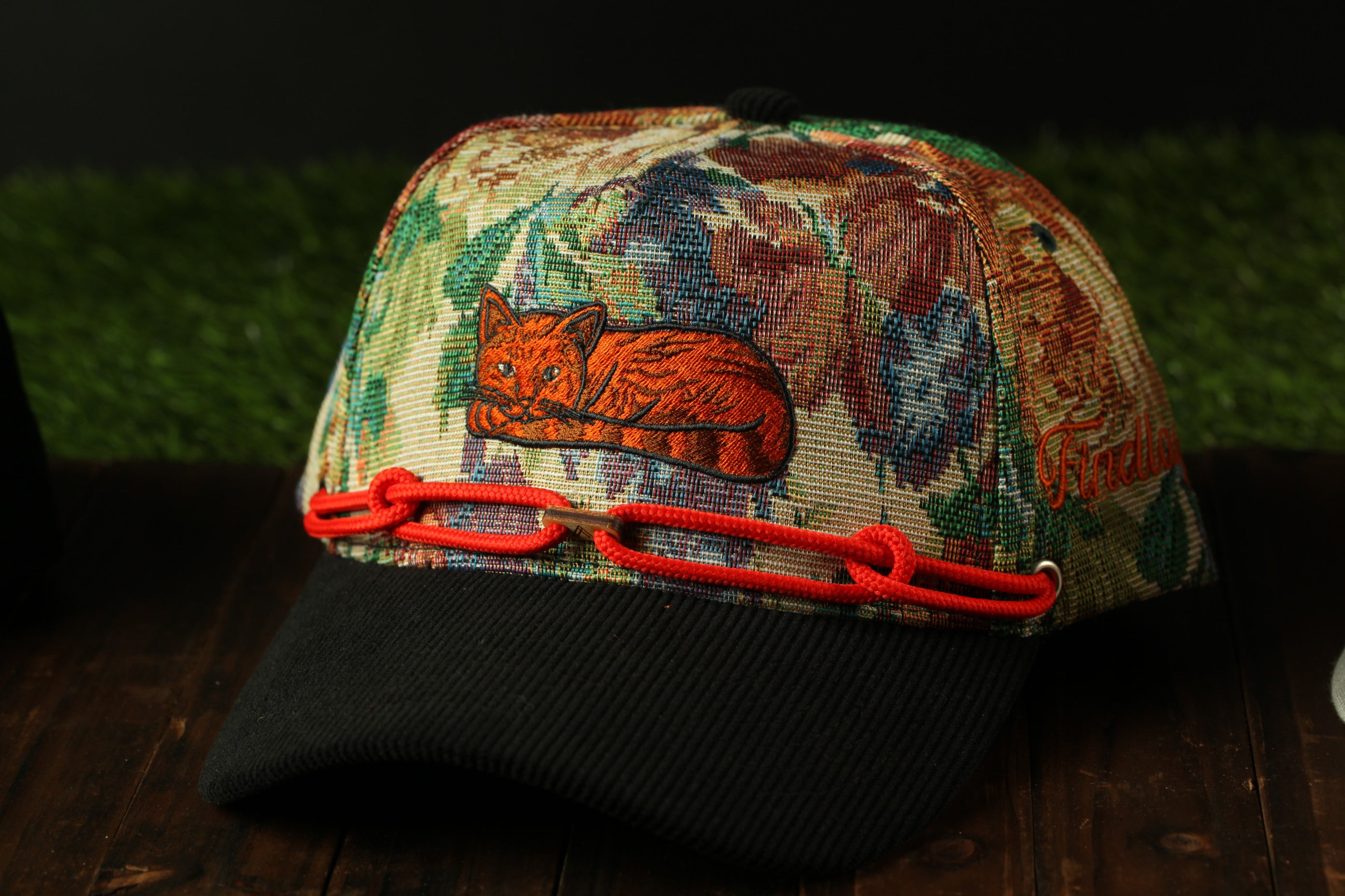 A colorful, patterned baseball cap with a cat embroidered on it, resting on a wooden surface.