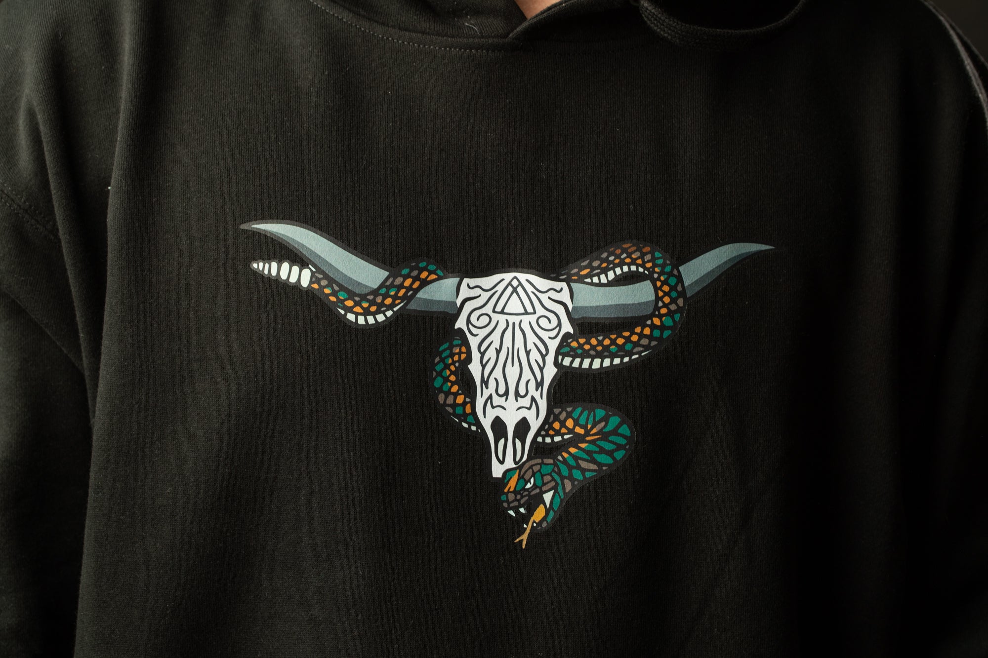 A black hoodie with a graphic design of a white skull with horns and a green snake wrapped around it.