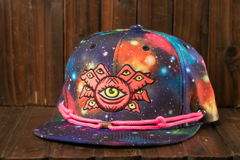 A colorful, patterned baseball cap with a unique design featuring a large eye-like symbol and a pink string around the brim.