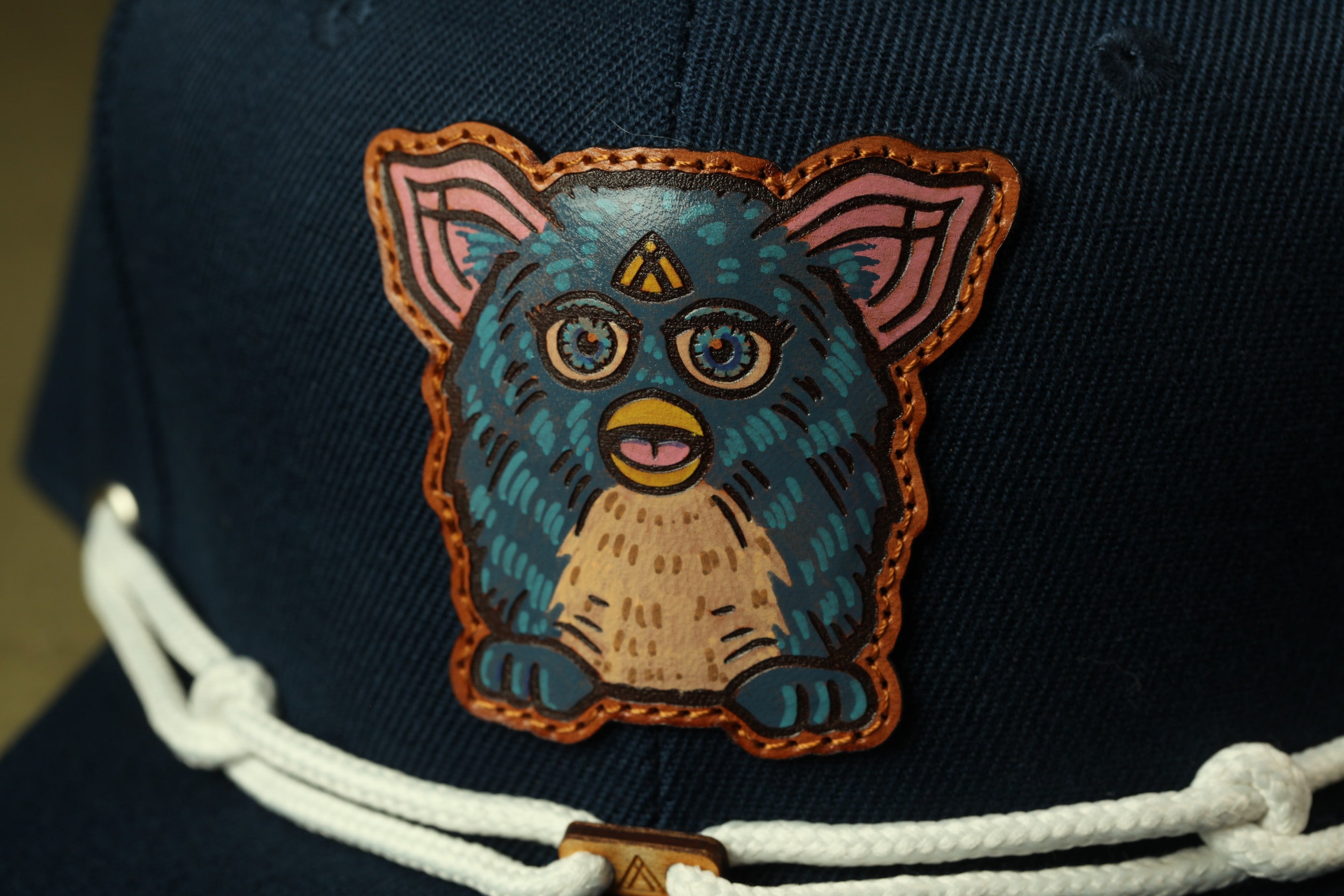 A close-up of a dark blue baseball cap with a colorful, cartoonish design of a blue and orange creature on the front.