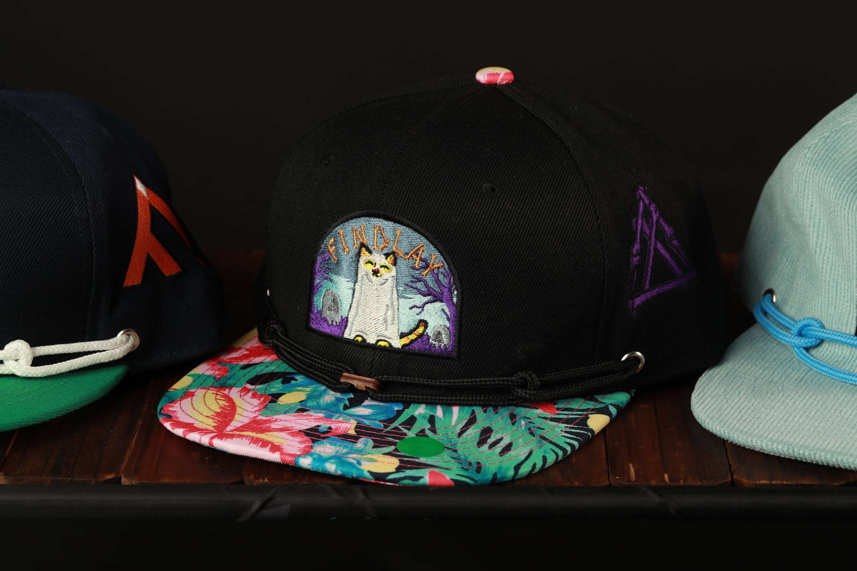 A collection of colorful baseball caps with various designs and patterns, including a black cap with a cat embroidered on it.