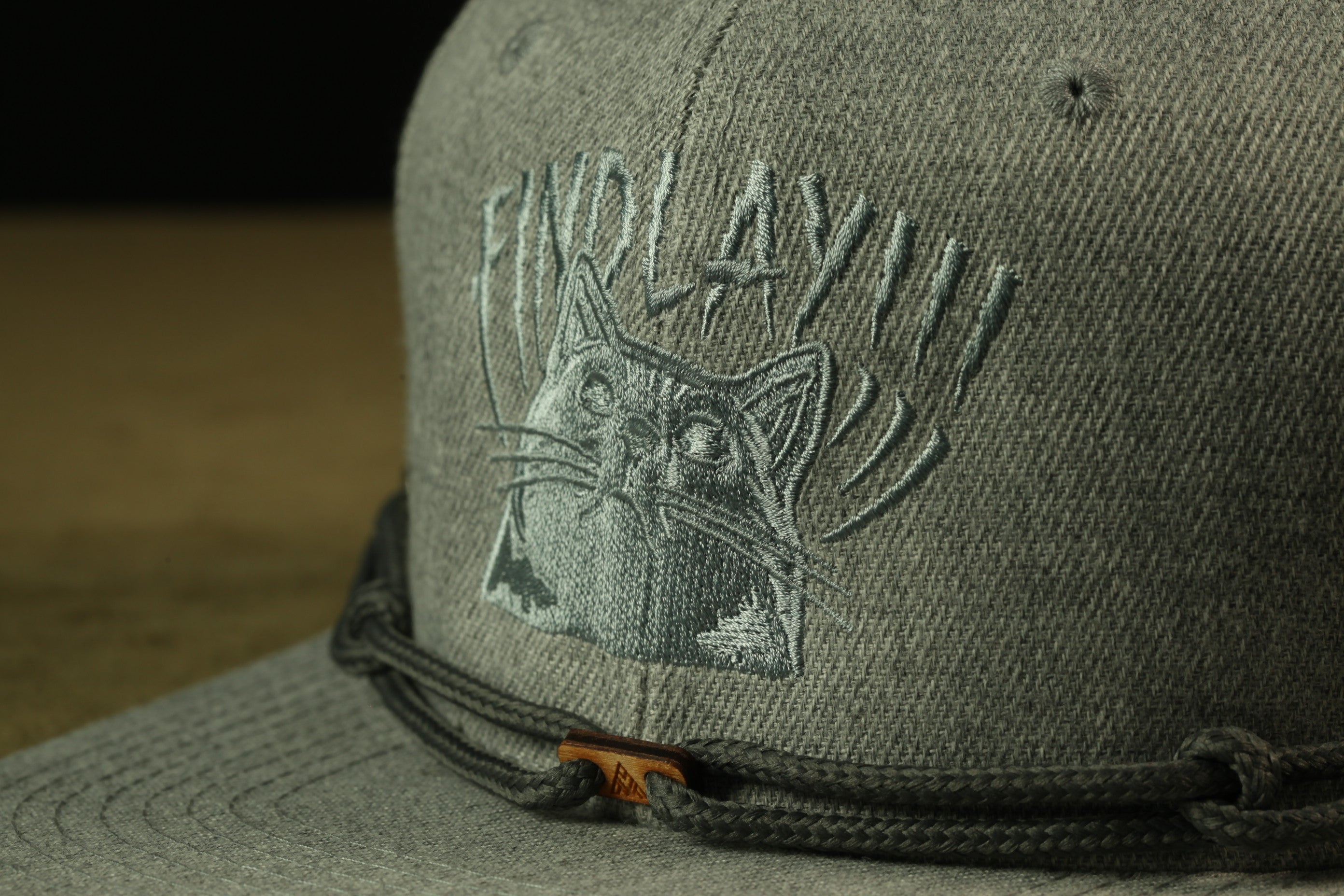 A close-up view of a gray baseball cap with a cat embroidered on it.