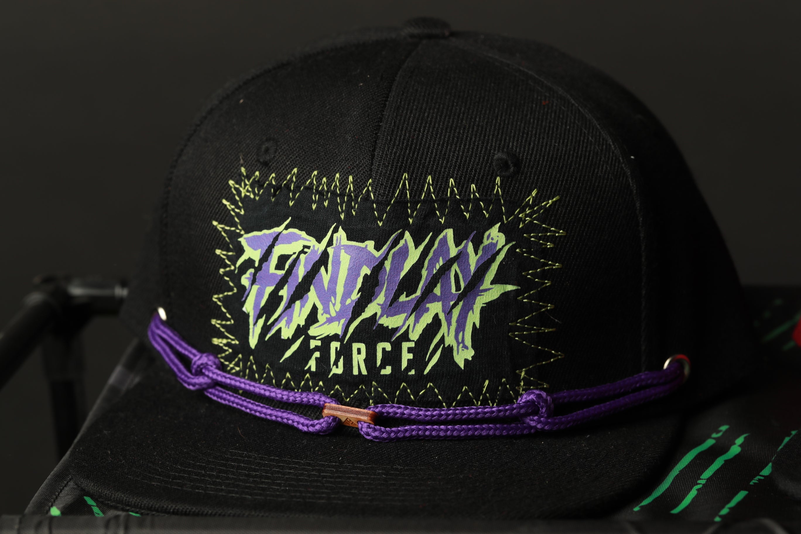 A black baseball cap with a purple and green graphic design on it.