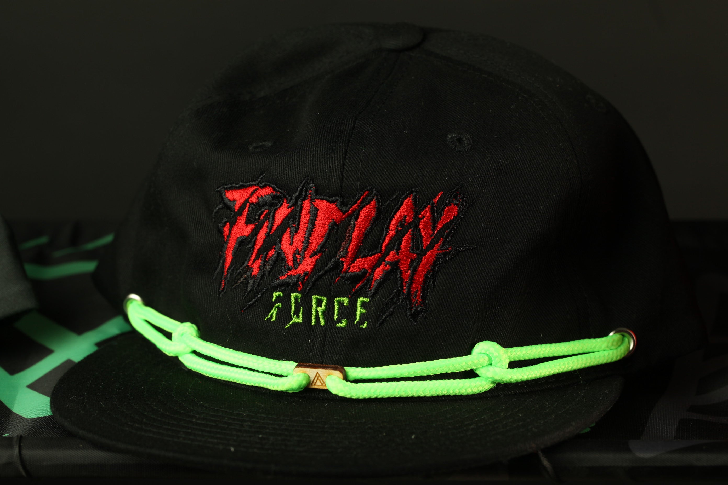 A black baseball cap with a green string and a red and black logo on it.