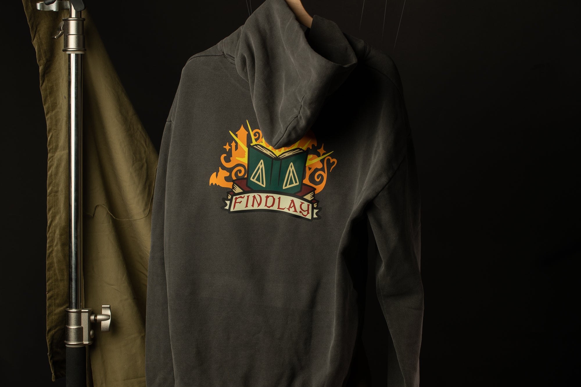 A grey hooded sweatshirt with a colorful graphic design on the back, hanging on a hanger against a dark background.