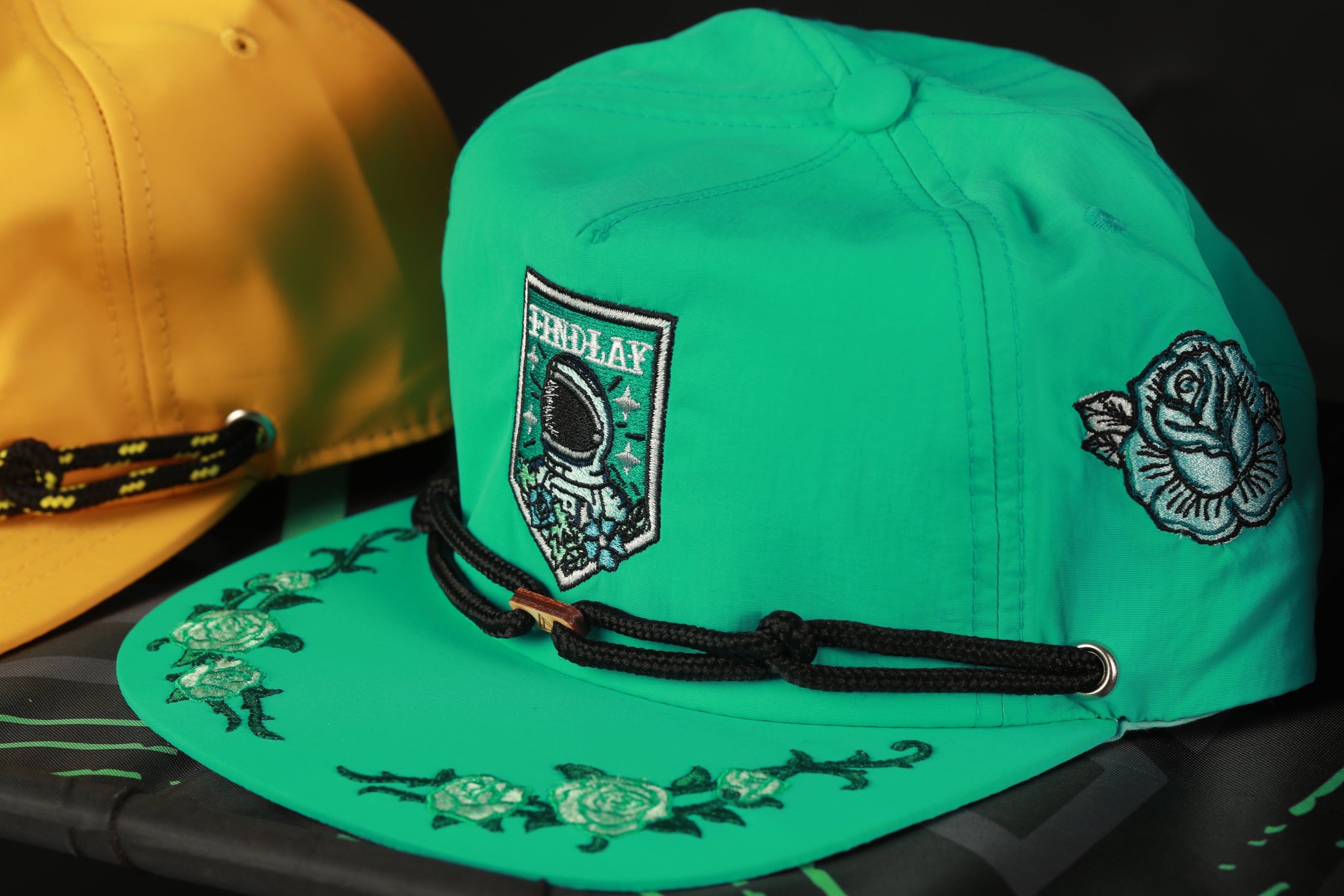 two baseball caps, one green and one yellow, with floral designs and patches on them.