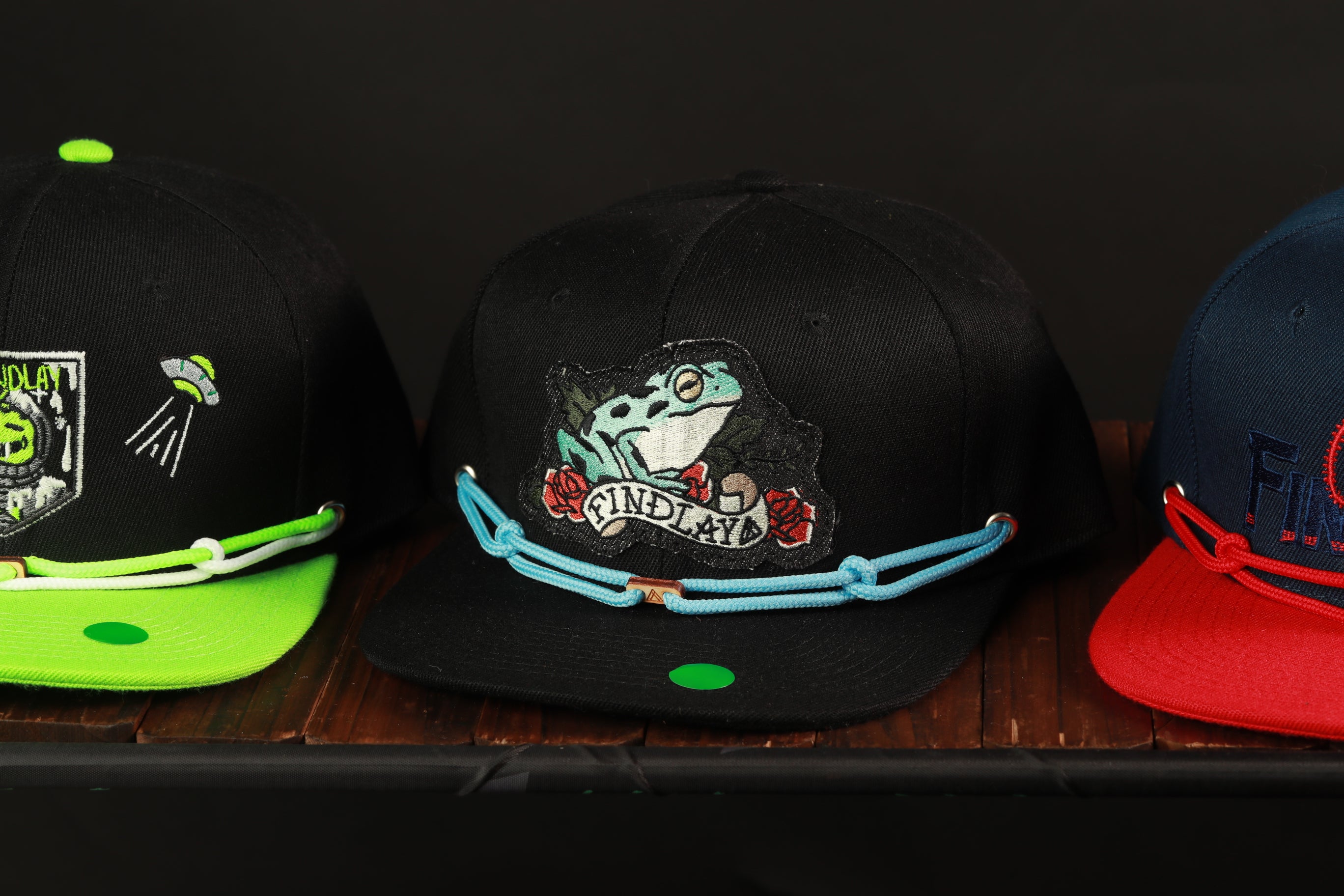 Three baseball caps with different designs and colors are displayed on a wooden surface.