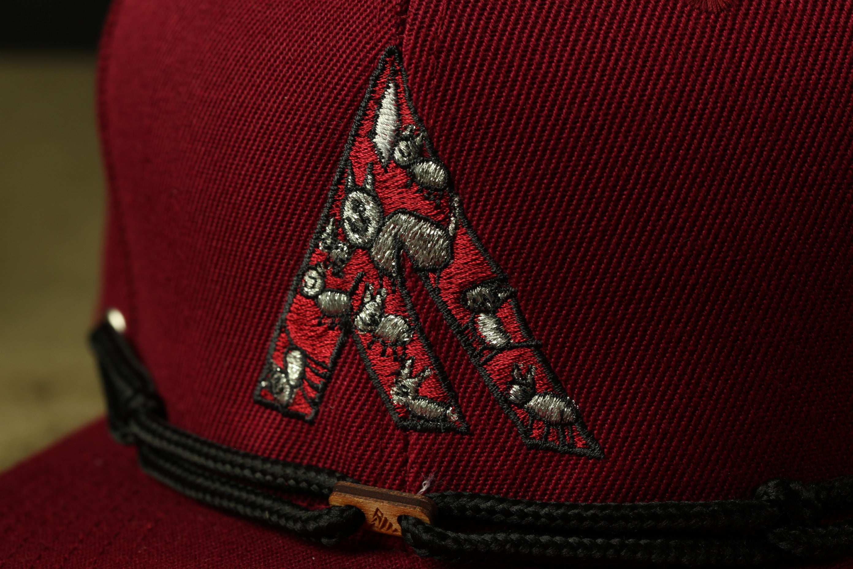 A close-up view of a red baseball cap with a black band and a decorative embroidered logo on the front.