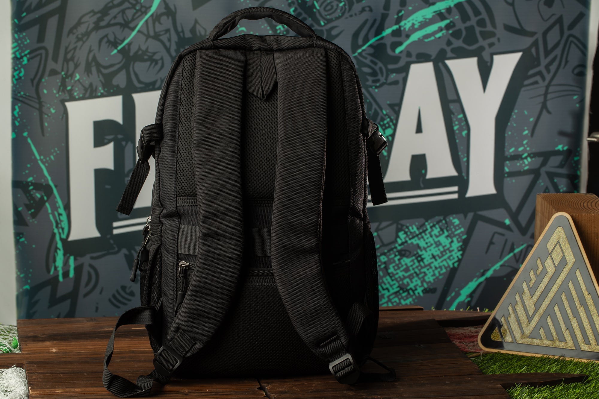 A black backpack is placed on a wooden surface, with a colorful graffiti-style background behind it.