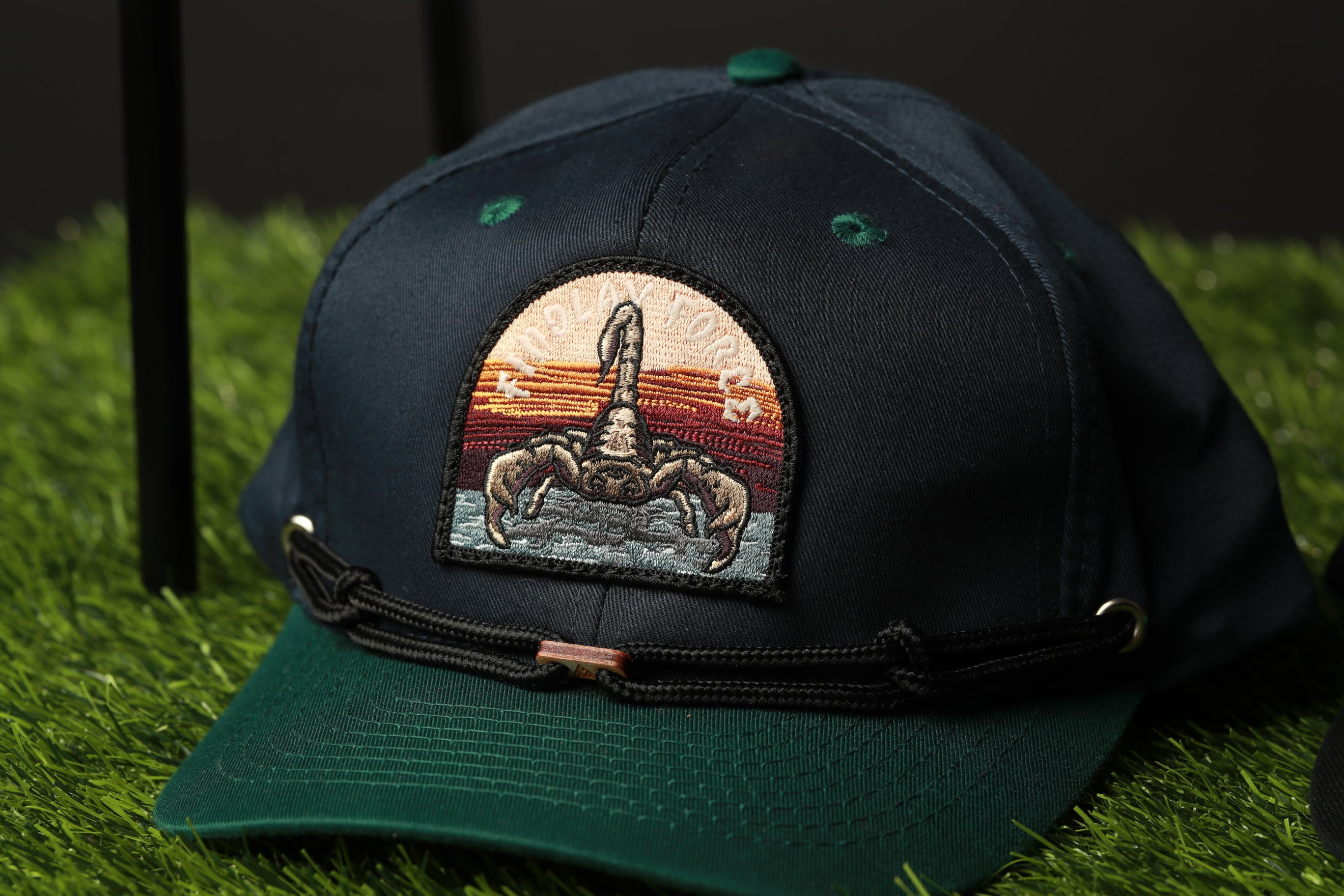 A dark green baseball cap with a colorful embroidered design on the front, featuring a stylized image of a person holding a snake.