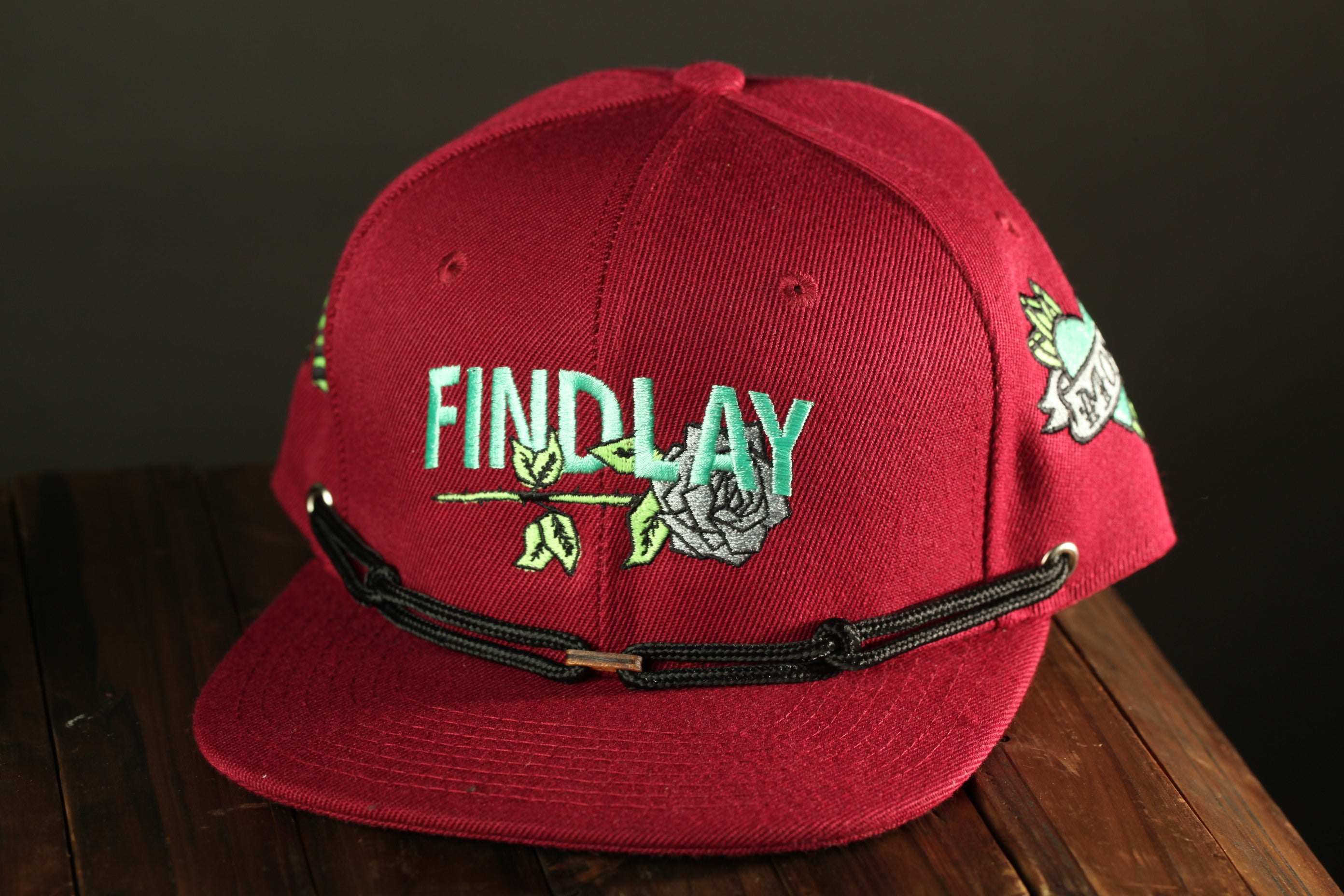 A red baseball cap with the word "FINDlay" printed on it, sitting on a wooden surface.