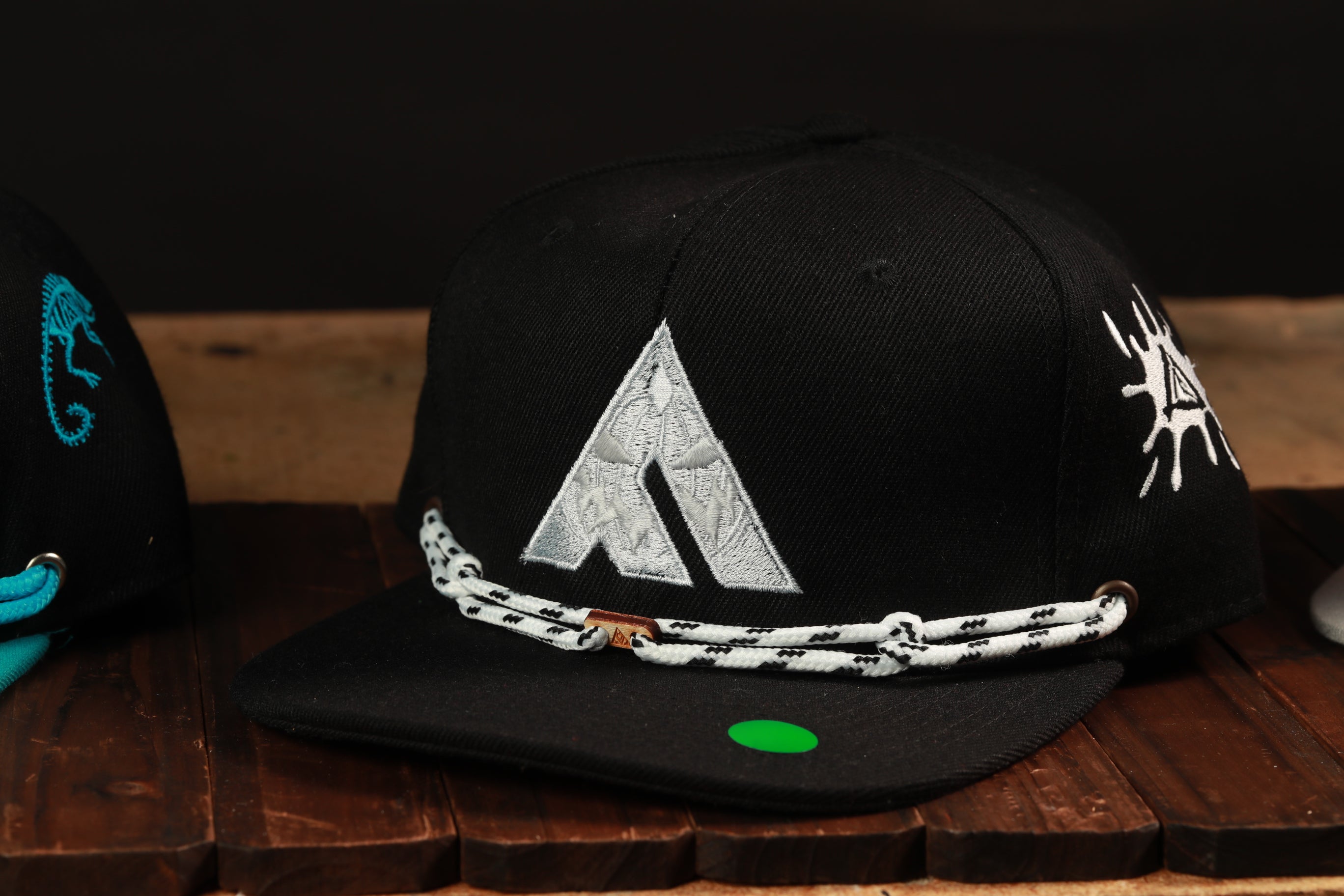 A black baseball cap with a white triangle logo and a green tag is displayed on a wooden surface.