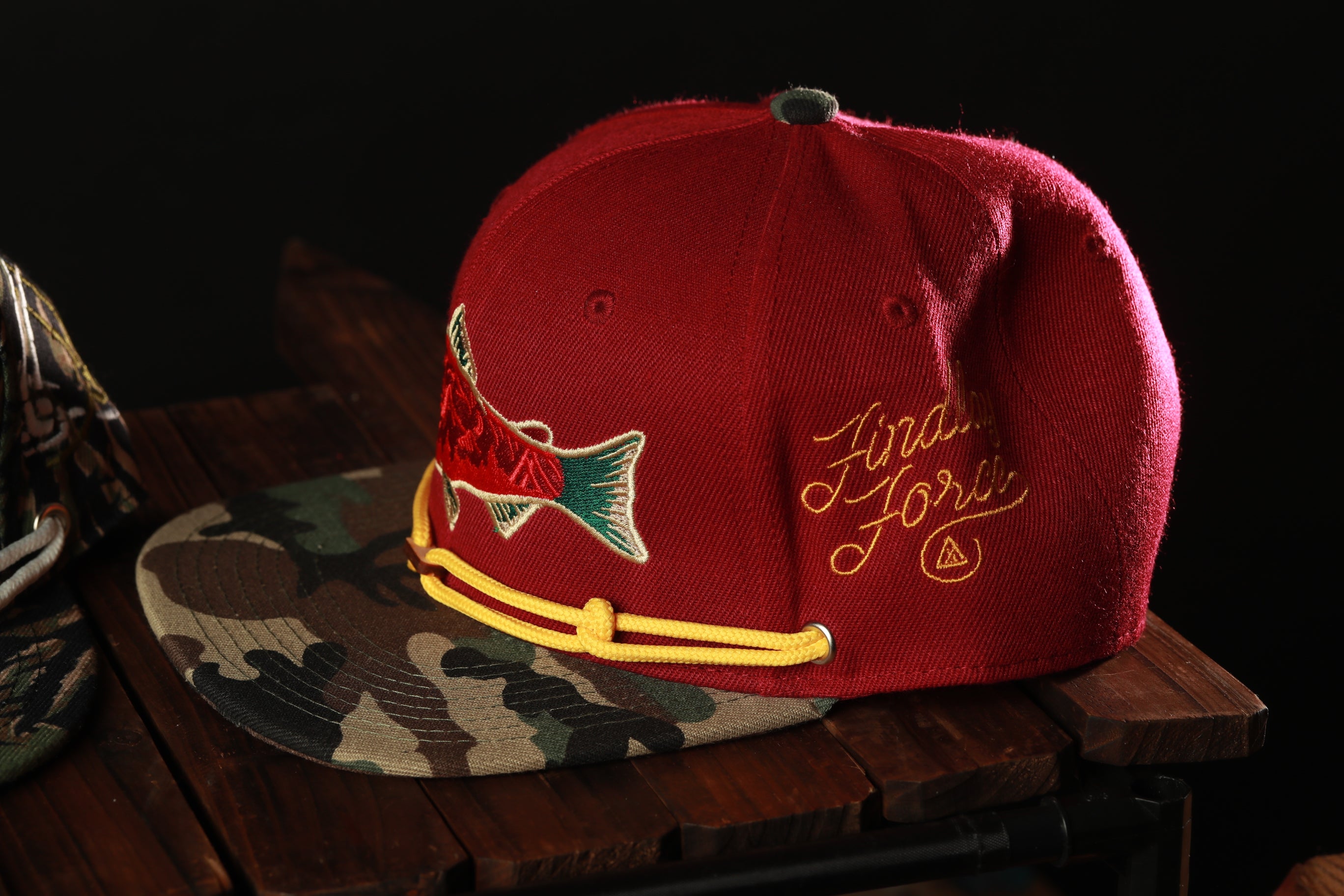 A red baseball cap with a fish embroidered on it, placed on a wooden surface.