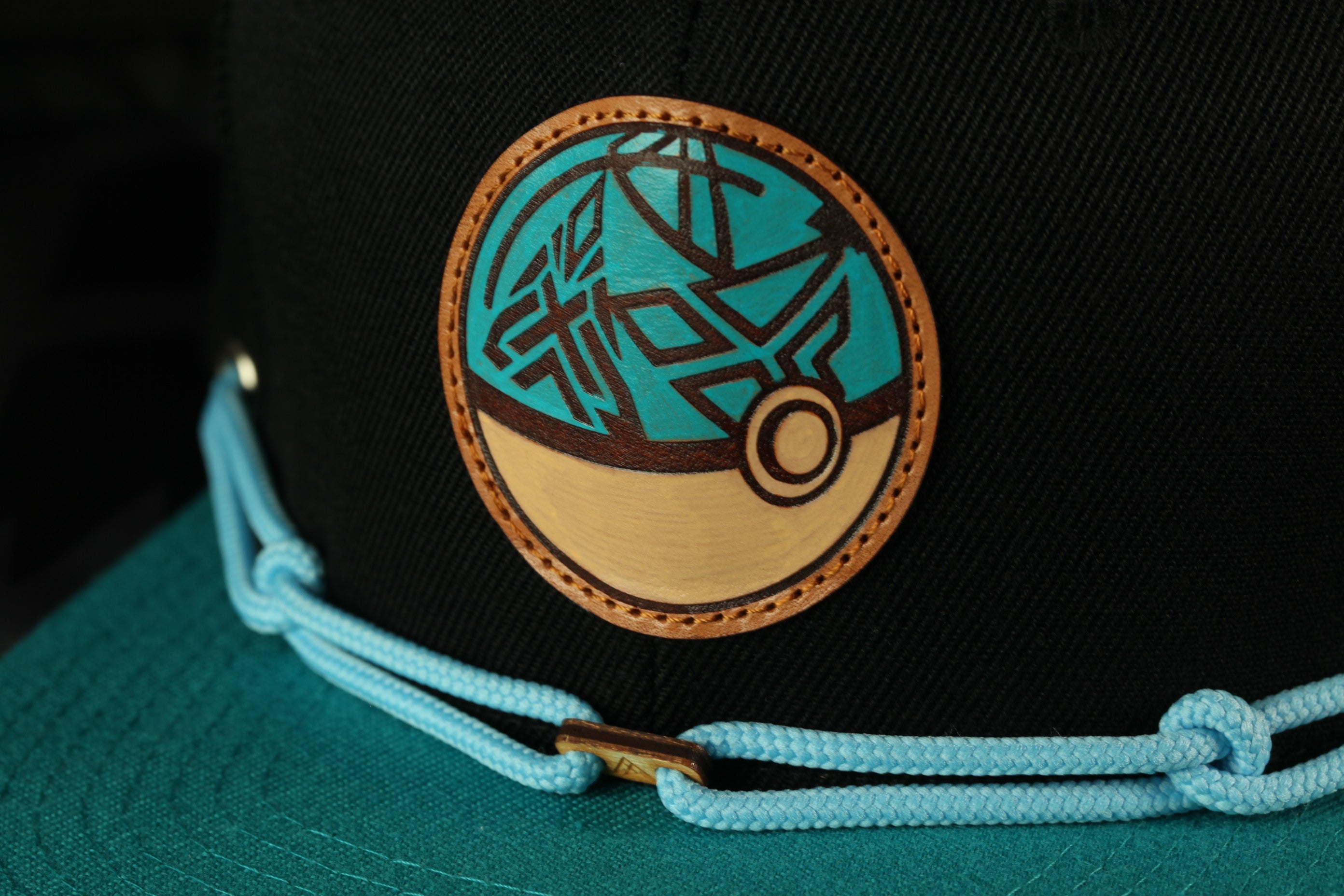 A close-up view of a black baseball cap with a blue and brown circular logo on the front.