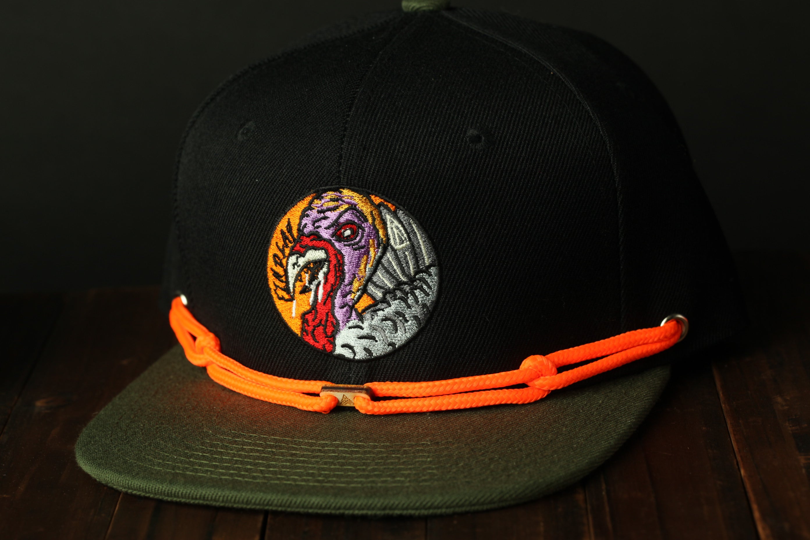 A black baseball cap with an orange and green band around it, featuring a colorful embroidered design on the front.